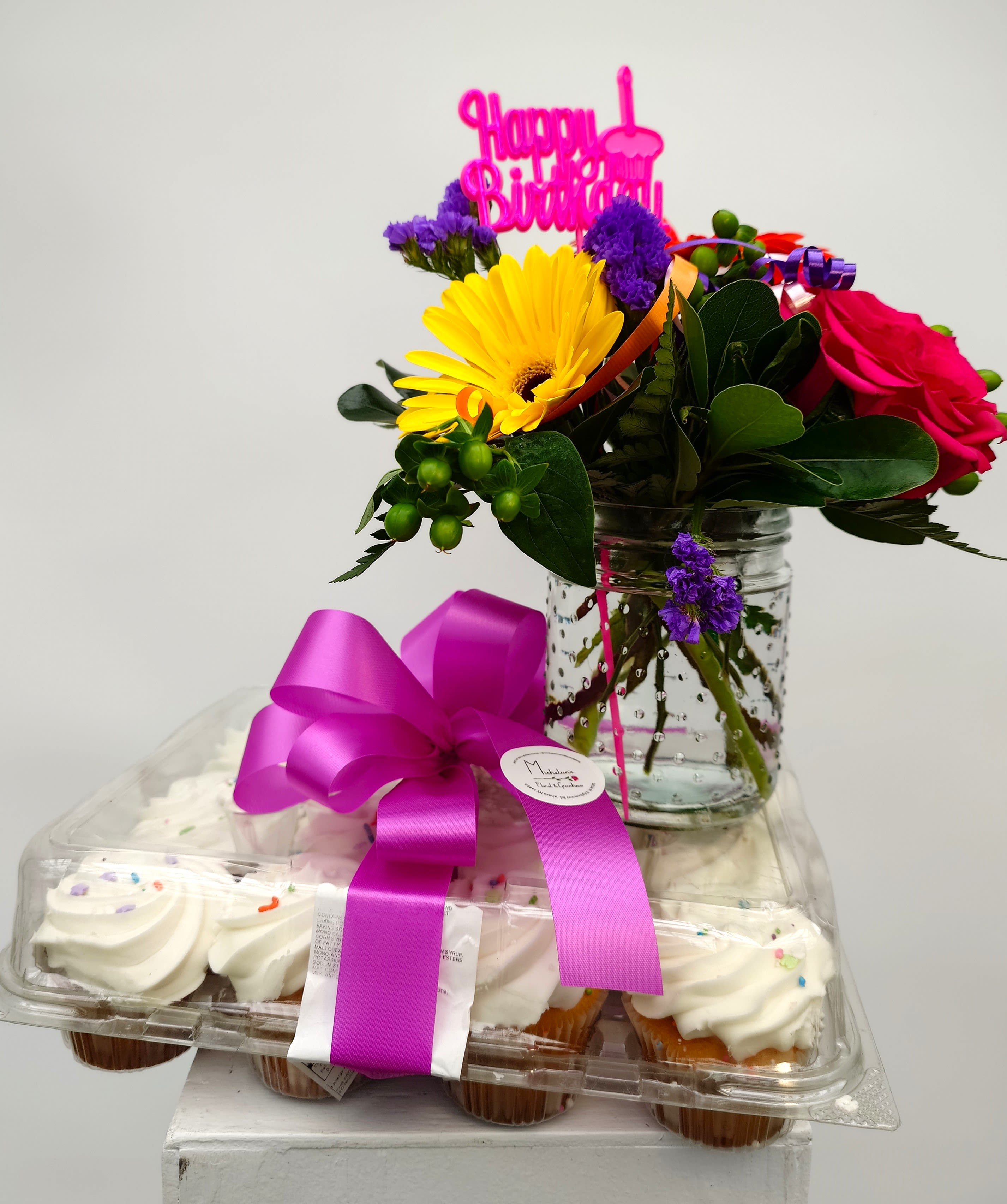 Birthday flower arrangement with cupcakes and a pink topper in a jar vase