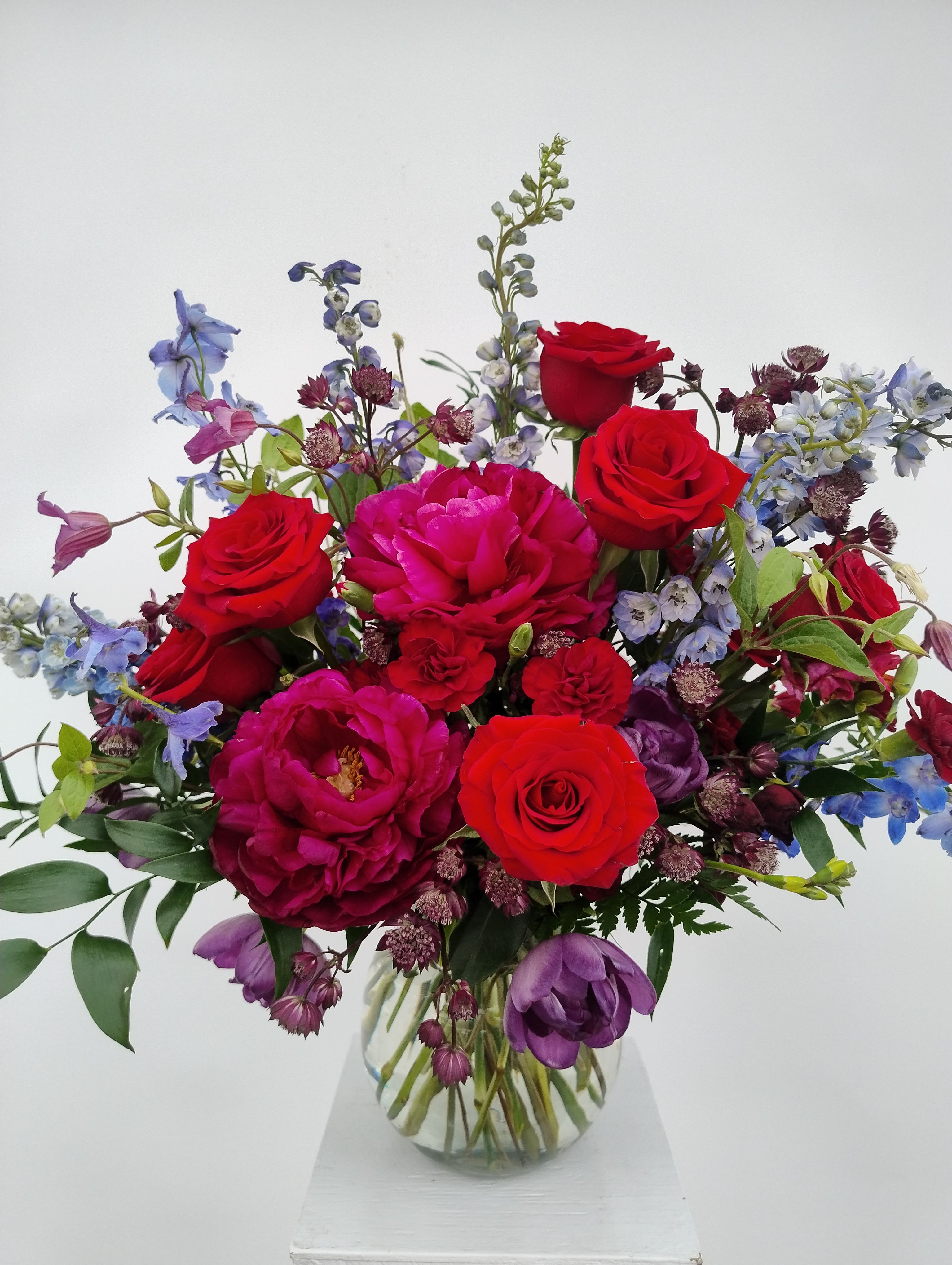Bouquet of red roses and purple flowers in a clear glass vase
