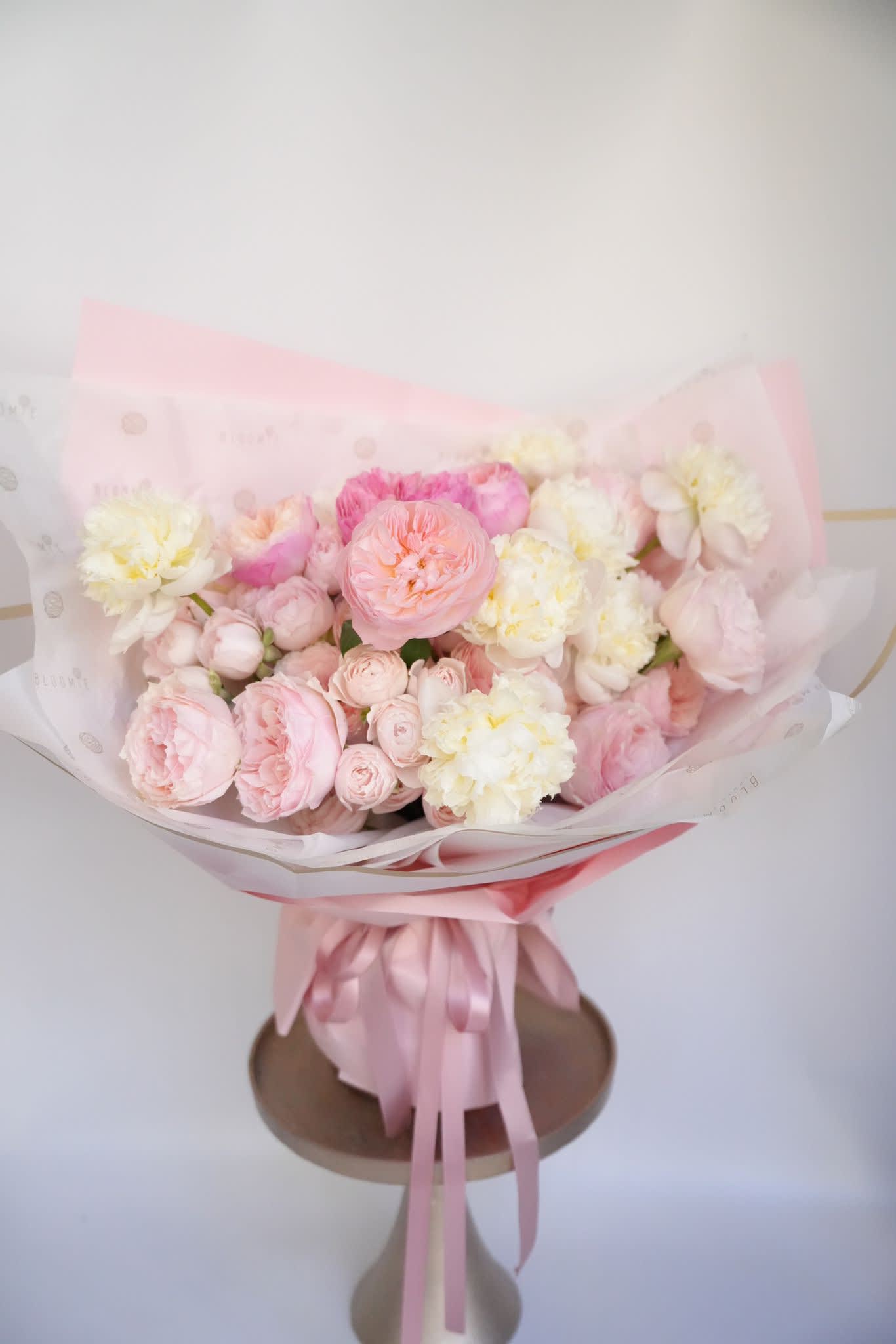 Round bouquet of pale pink and cream roses and peonies in a pink hatbox with ribbon