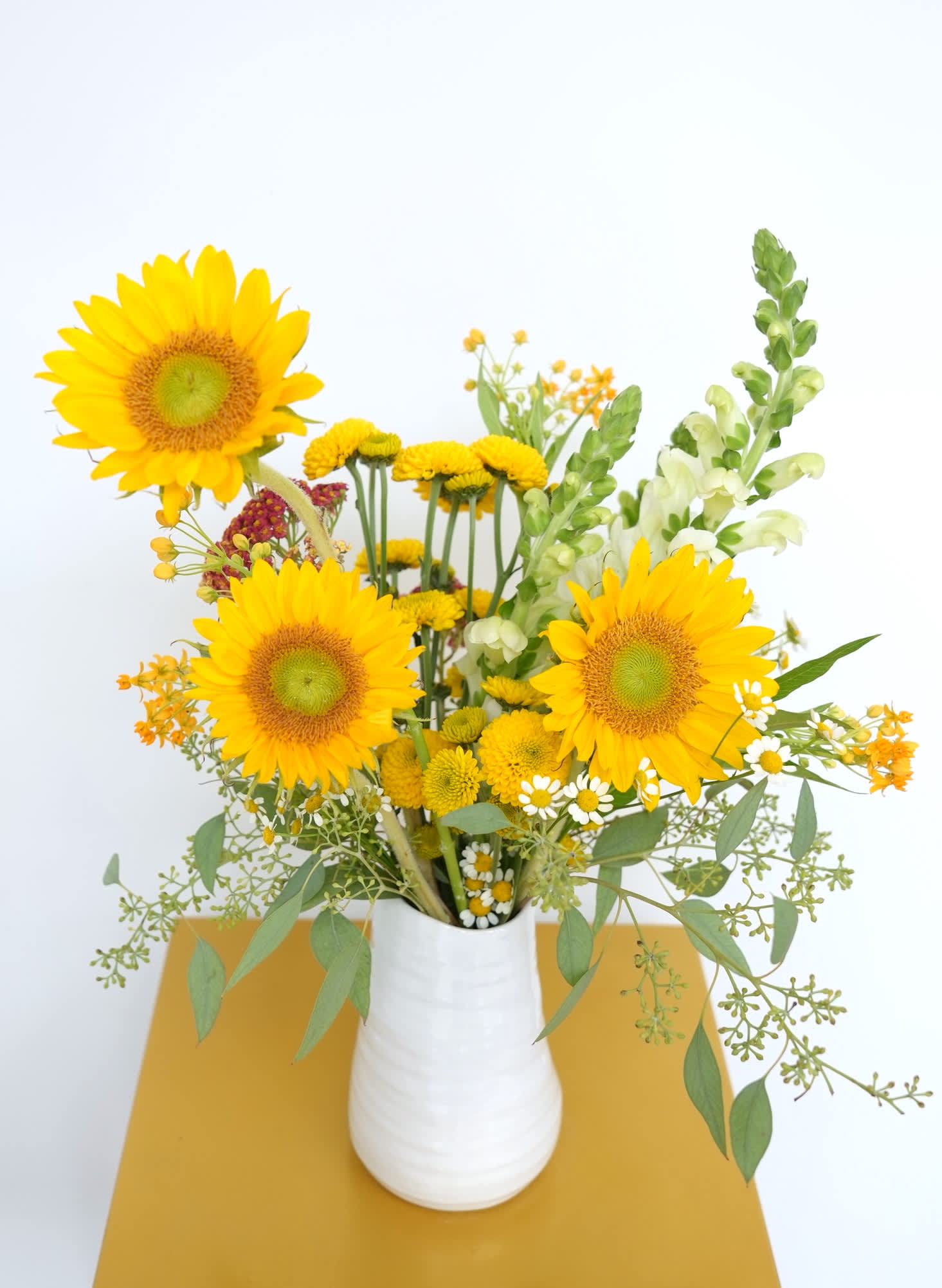 Yellow sunflower bouquet in a white vase with mixed small blooms