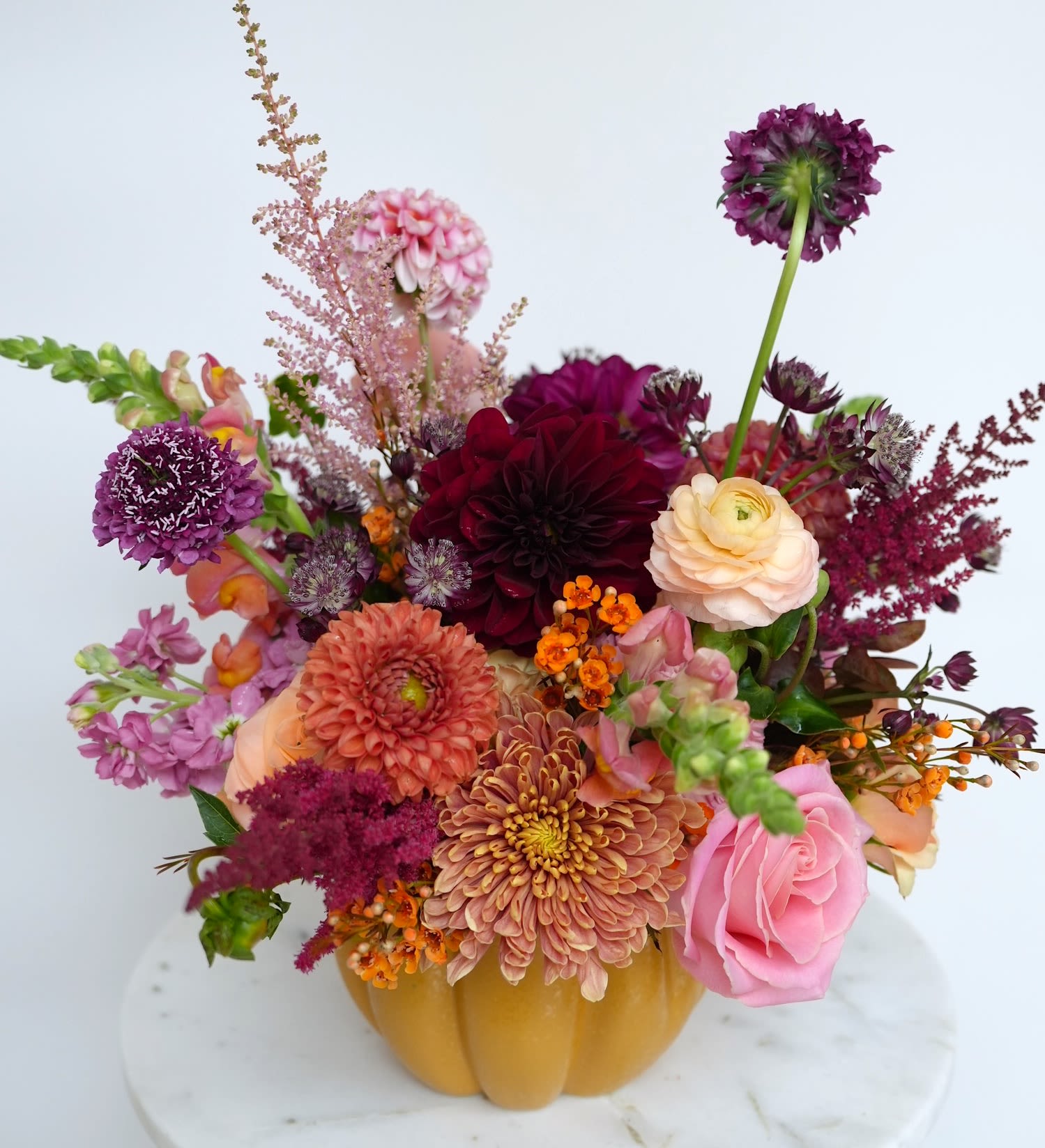 Mixed bouquet in a pumpkin-shaped vase with pink, purple, peach, and orange blooms.