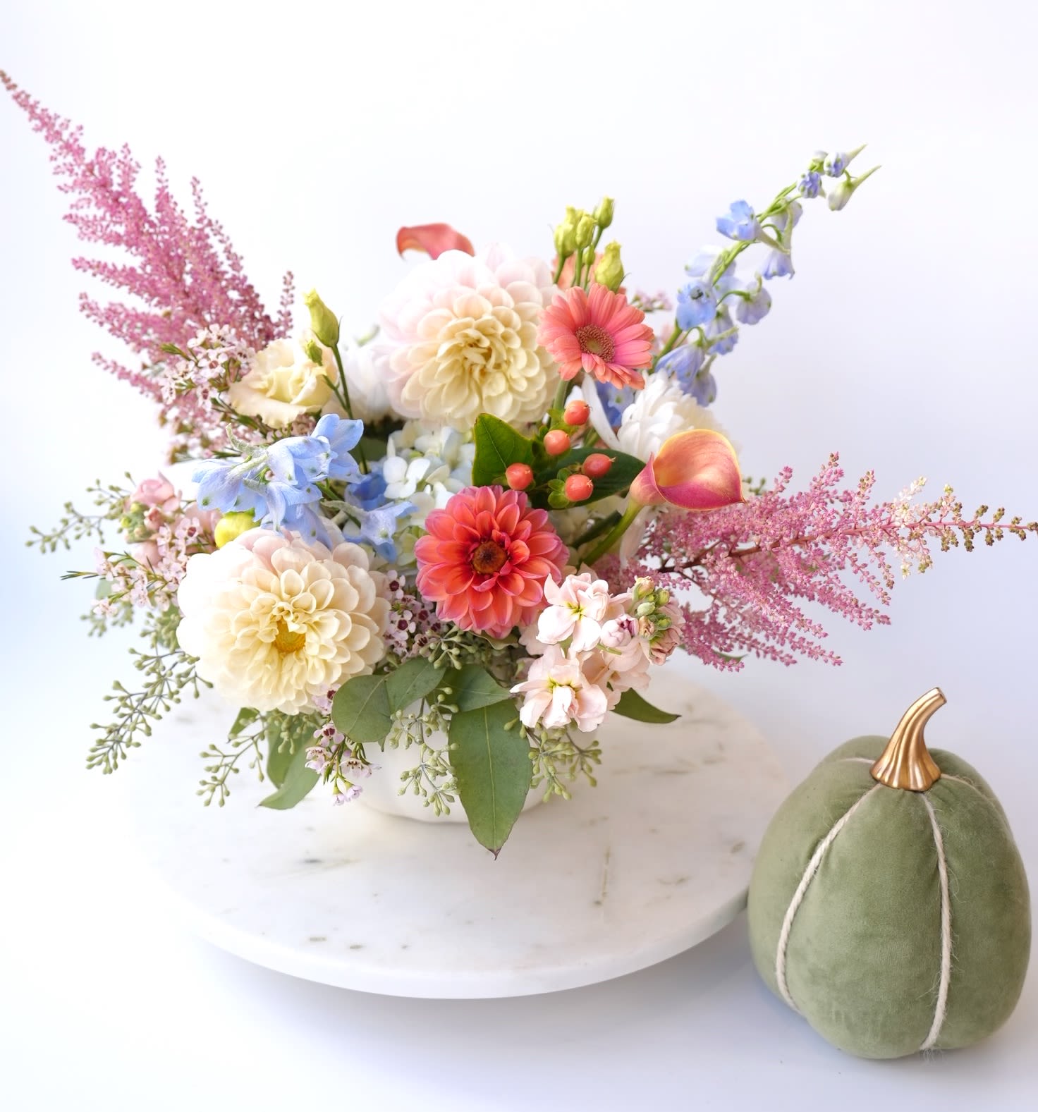 Mixed pastel flower arrangement in a white bowl with a green velvet pumpkin
