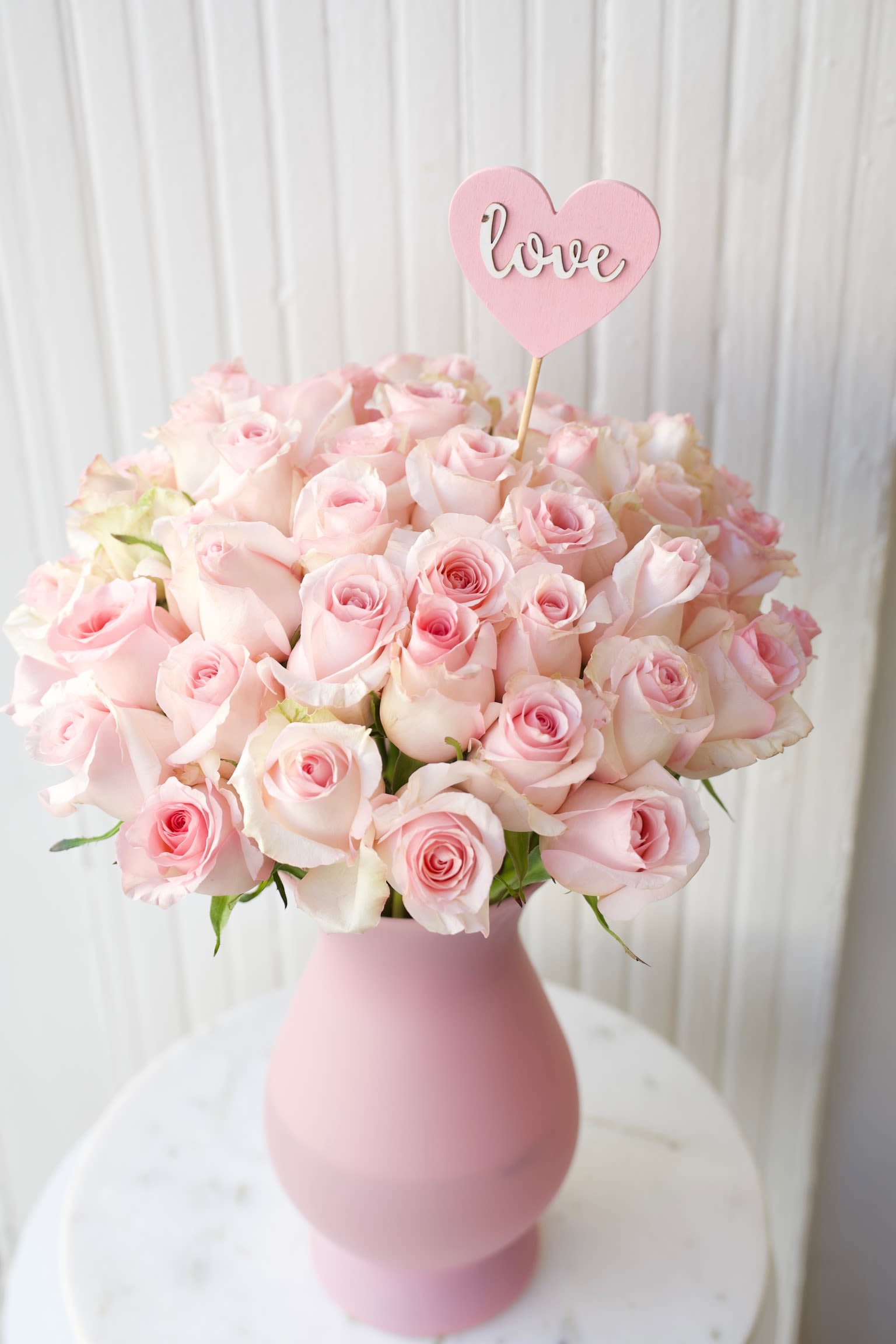 Pink rose bouquet in a matte pink vase with a heart-shaped love pick