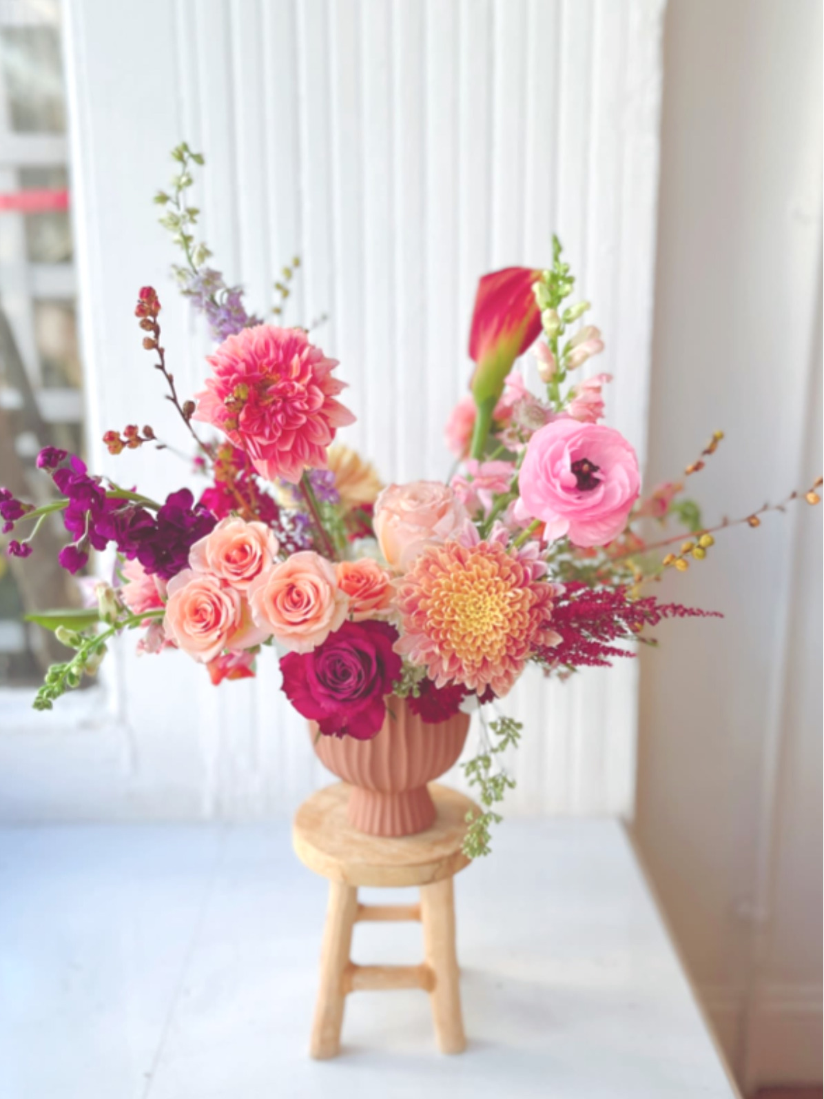 Fall Dreams - A vibrant fall arrangement featuring dahlias, roses, ranunculus, and mums in warm peach, coral, and pink tones. Designed in a ribbed clay vase, it adds a modern, elegant touch to your table or makes a thoughtful hostess gift.  