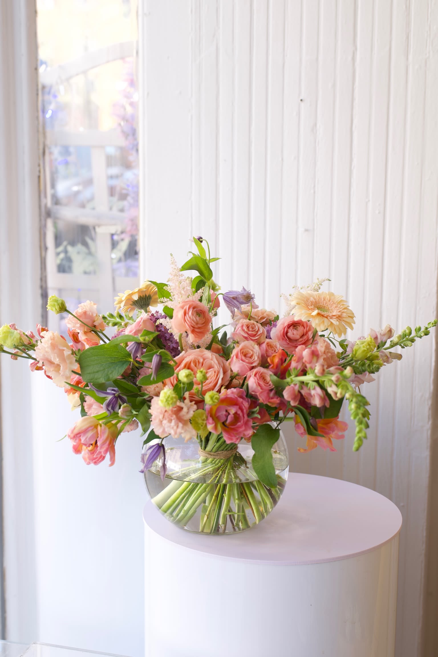 Peach &amp; Blush - An airy, garden-style floral arrangement featuring peach garden roses, ranunculus, tulips, snapdragons, and seasonal blooms in soft coral, blush, and fresh green tones. Designed in a low glass vase with a natural, organic shape, this elegant spring centerpiece brings a fresh, modern garden feel to any space.