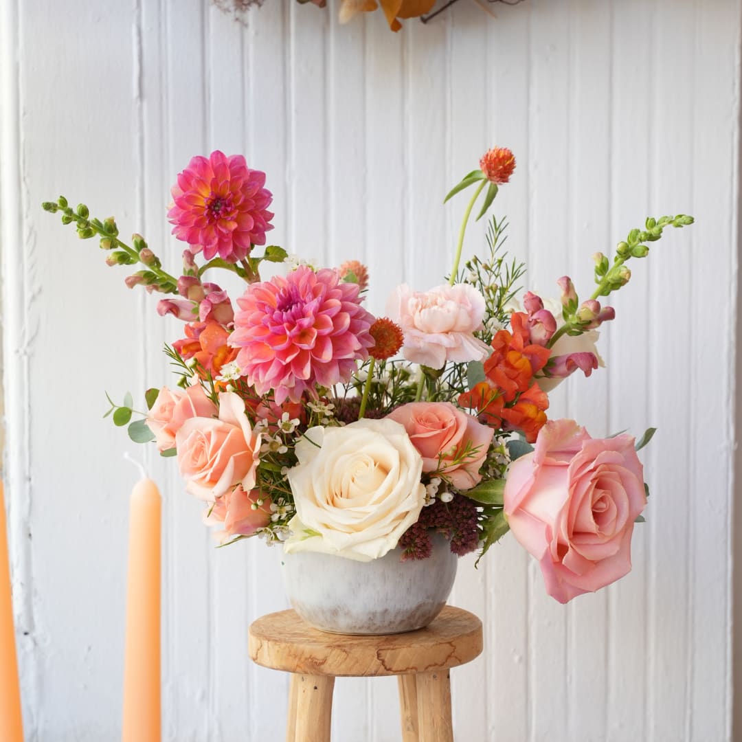 Pink and peach flowers arranged in a white vase on a stool