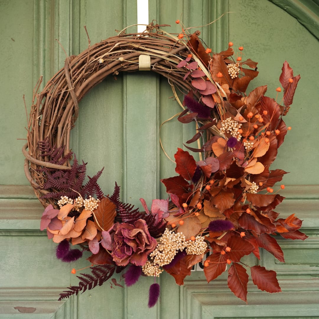 Autumn wreath with dried leaves, berries, and a grapevine base on a green door