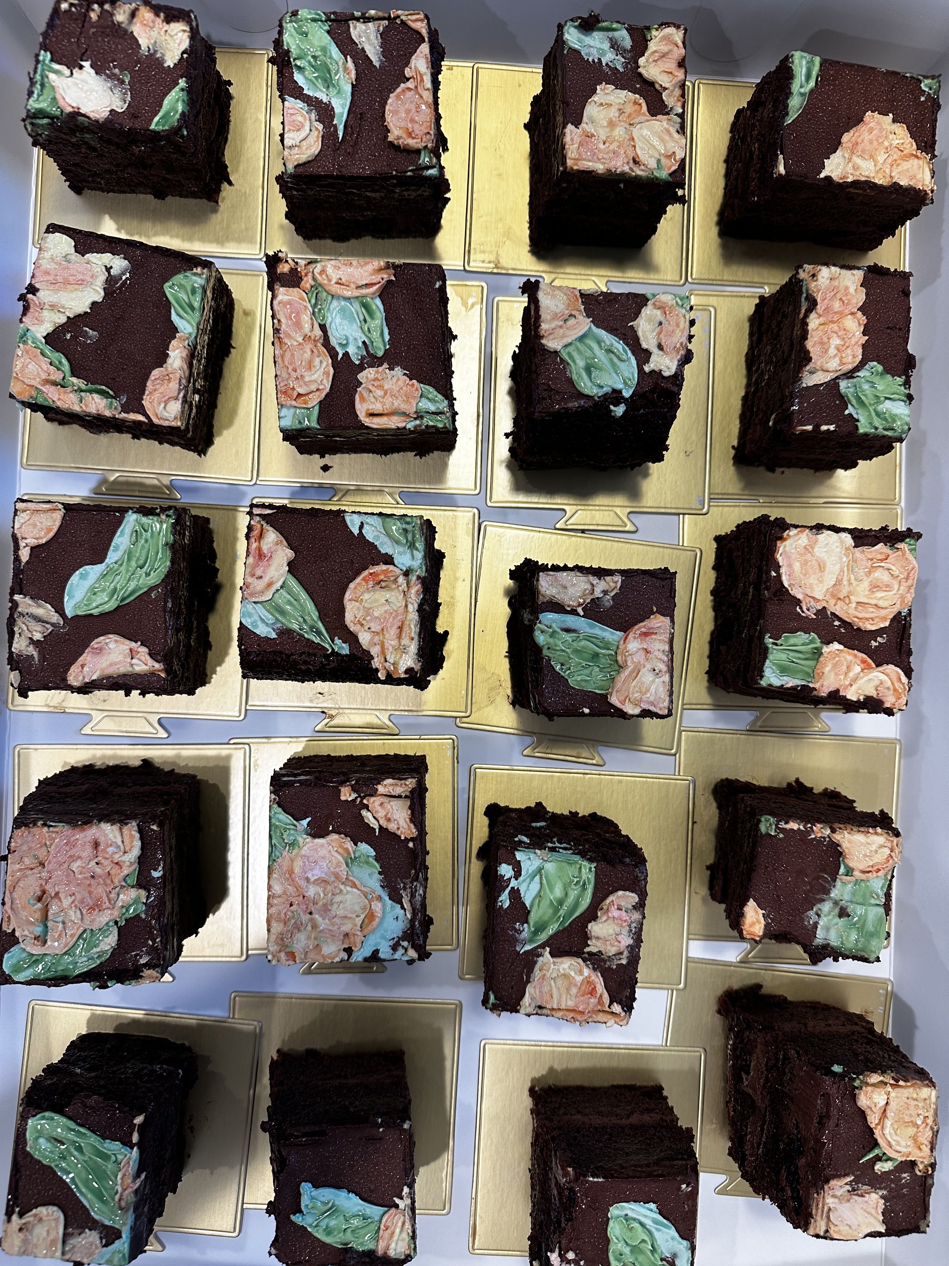 Square chocolate cakes topped with pastel floral frosting on gold boards