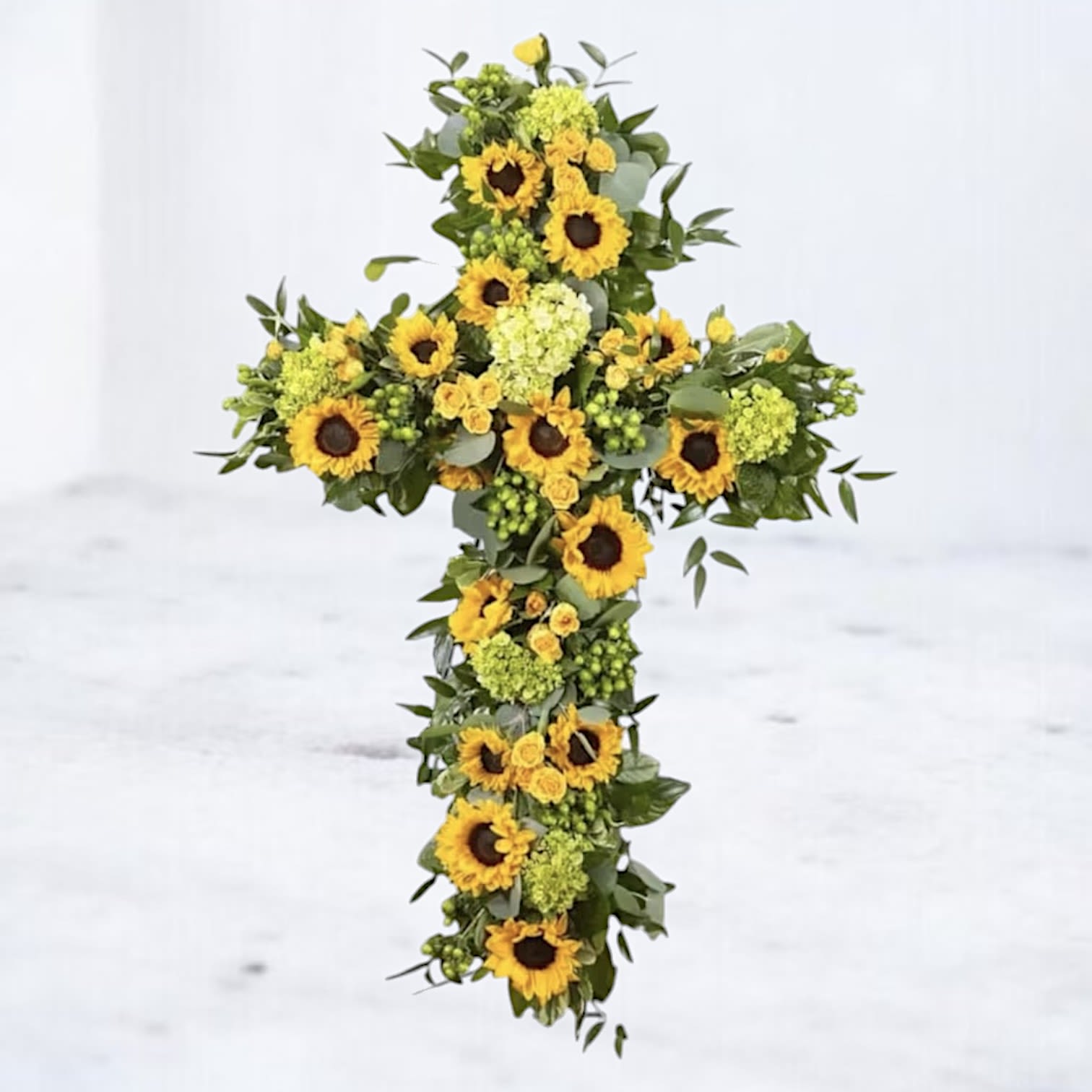 Sunflower cross arrangement with green filler on a white background