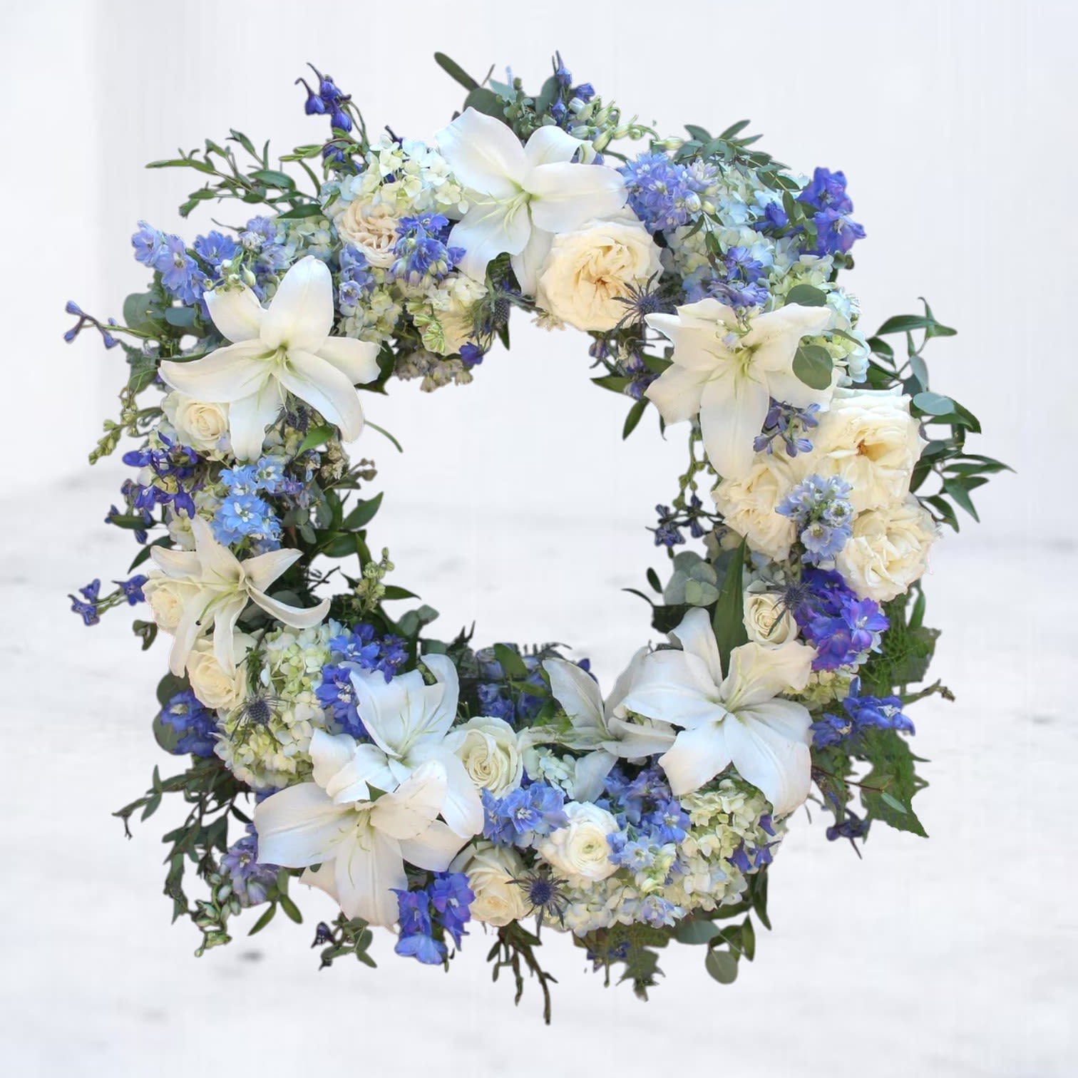 Floral wreath with white lilies, cream roses, and blue flowers
