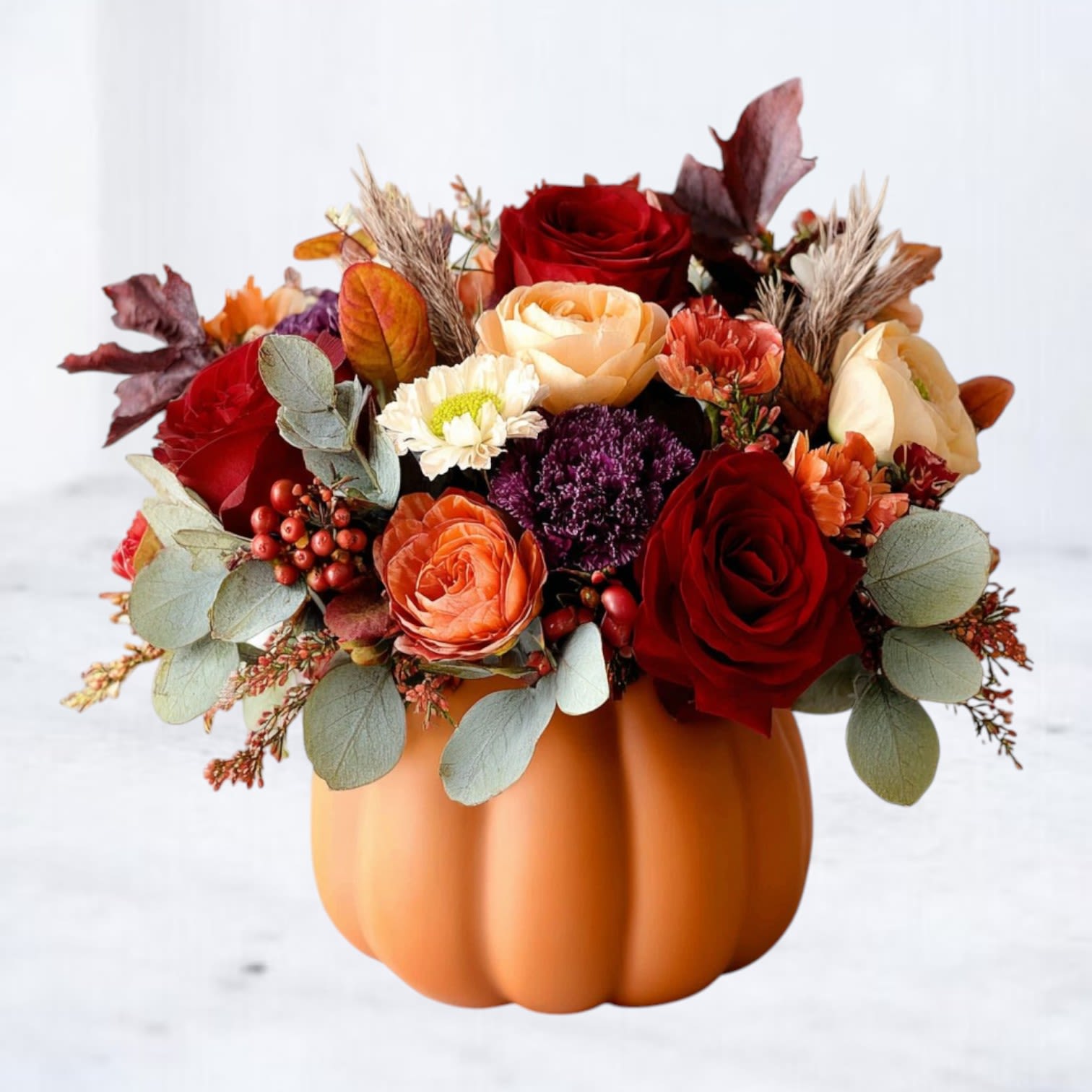 Fall floral arrangement in a pumpkin-shaped container with red and peach roses