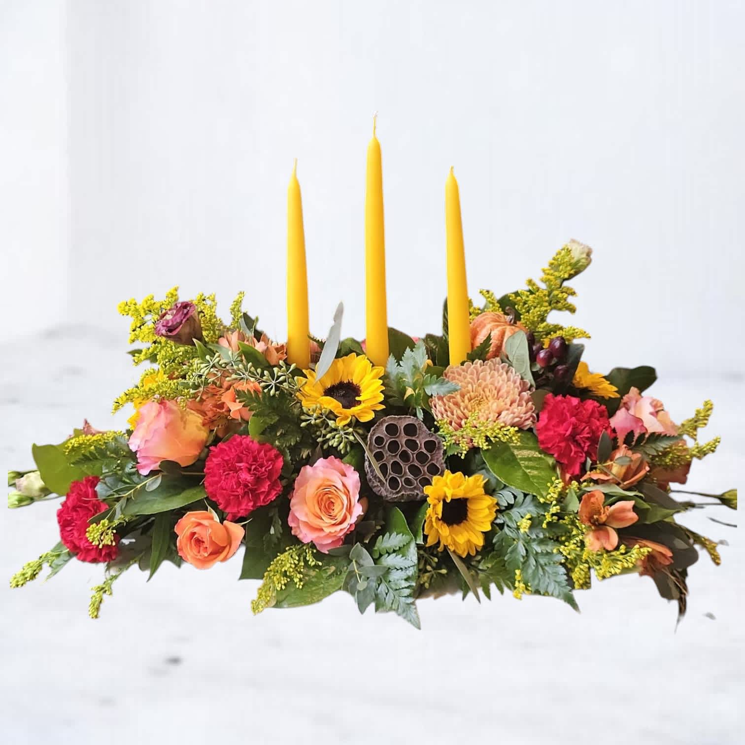 Low floral centerpiece with yellow taper candles and mixed blooms