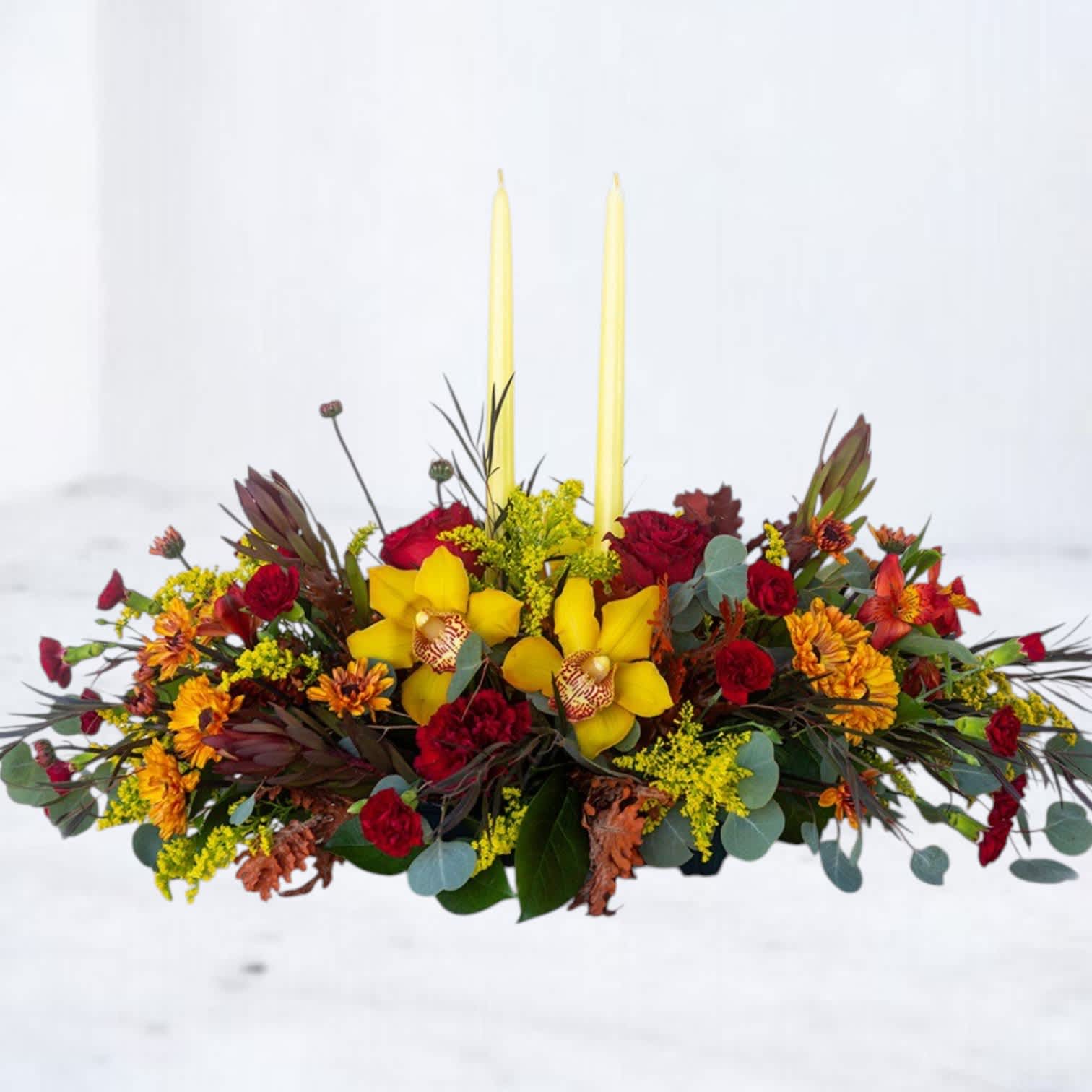 Low floral centerpiece with yellow orchids, red roses, and two tall candles