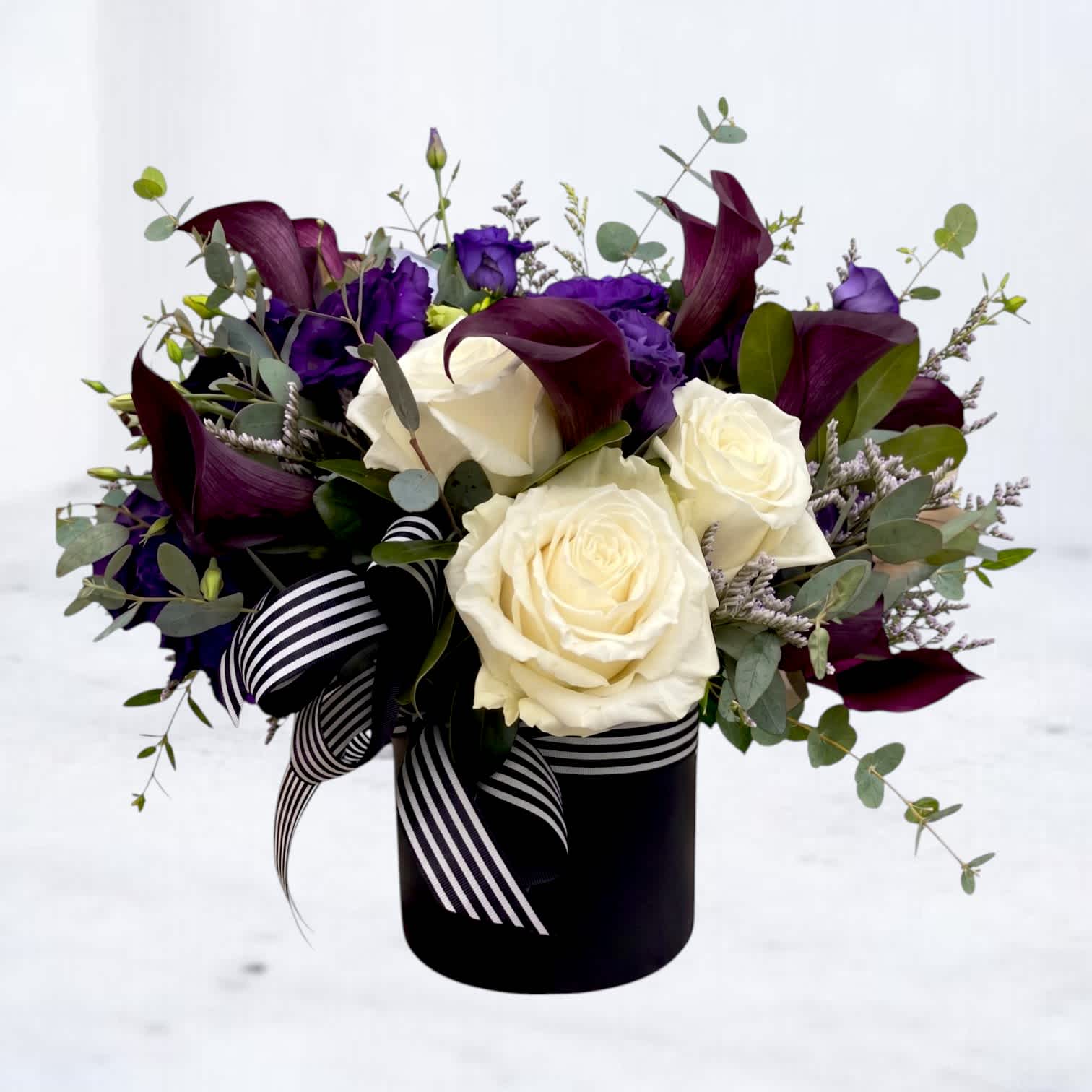 Bouquet of white roses, purple flowers, and dark calla lilies in a black vase