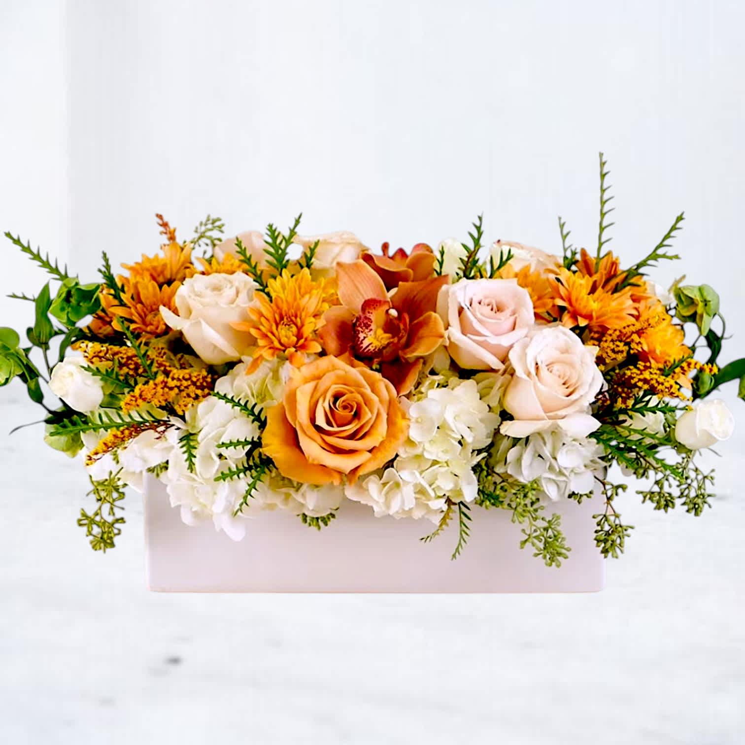 Low floral arrangement with orange and white roses in a pale rectangular box