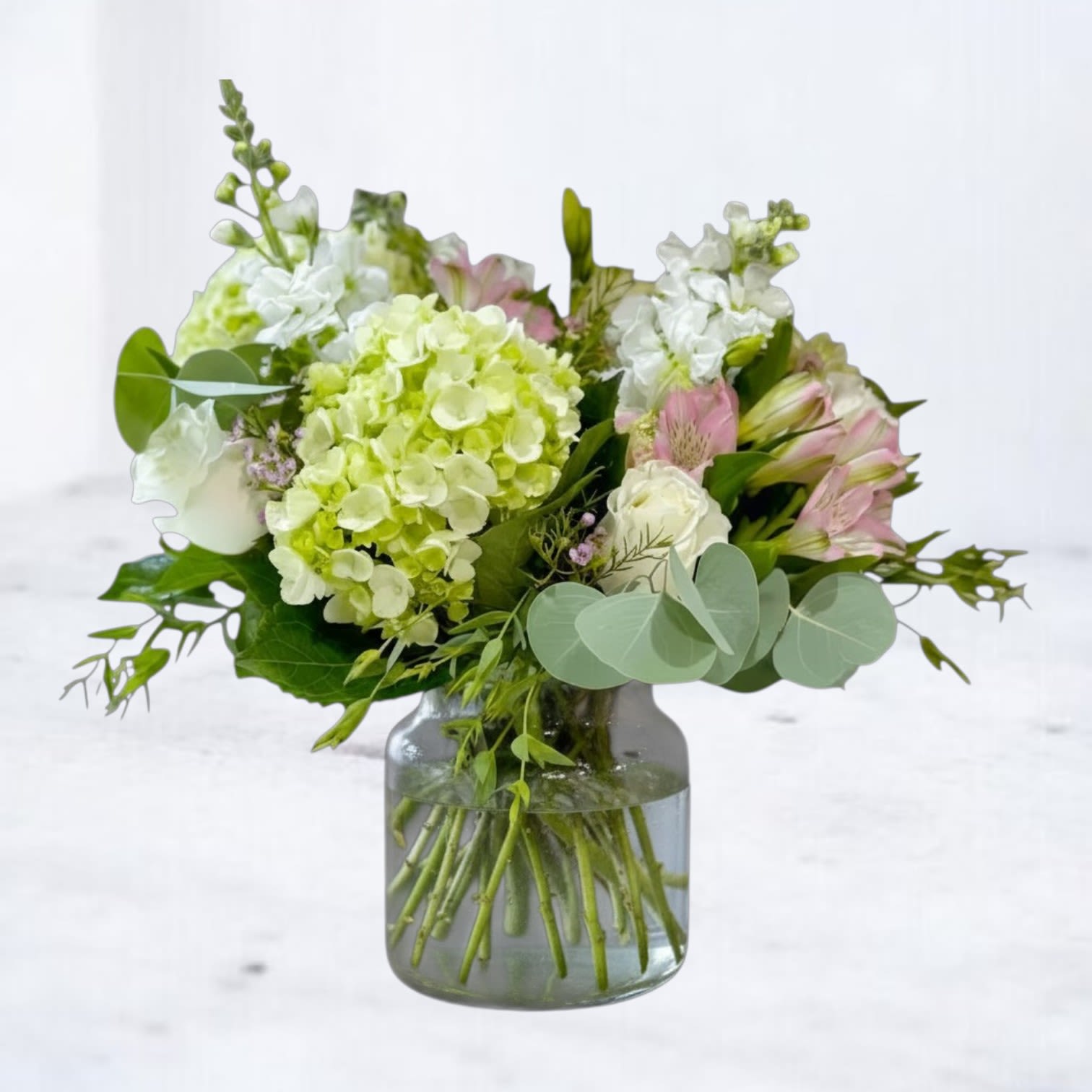Short mixed bouquet of green hydrangea, white roses, and pink alstroemeria in a clear glass jar vase.