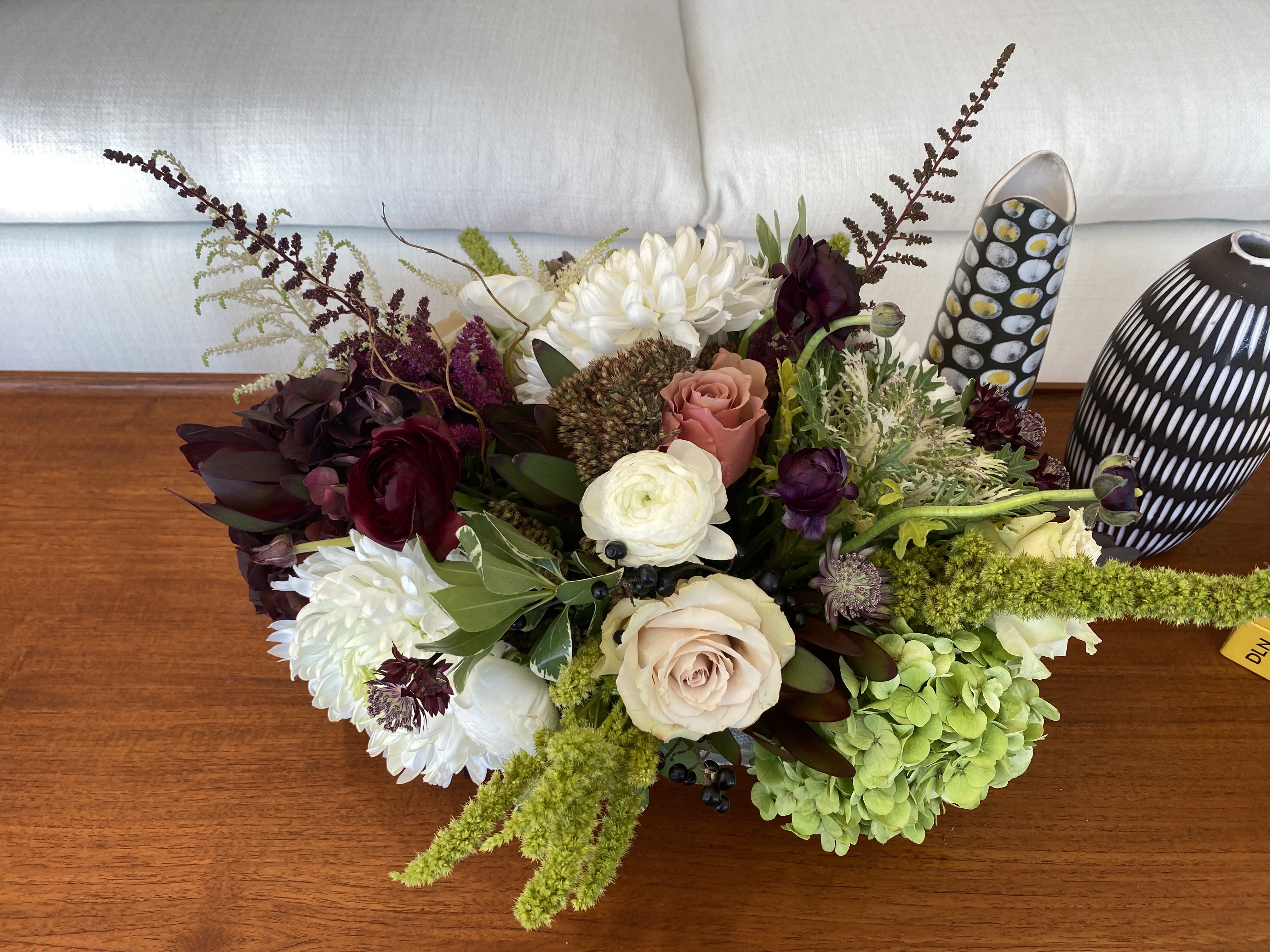 Low floral arrangement with white, blush, burgundy, and green blooms in decorative vases