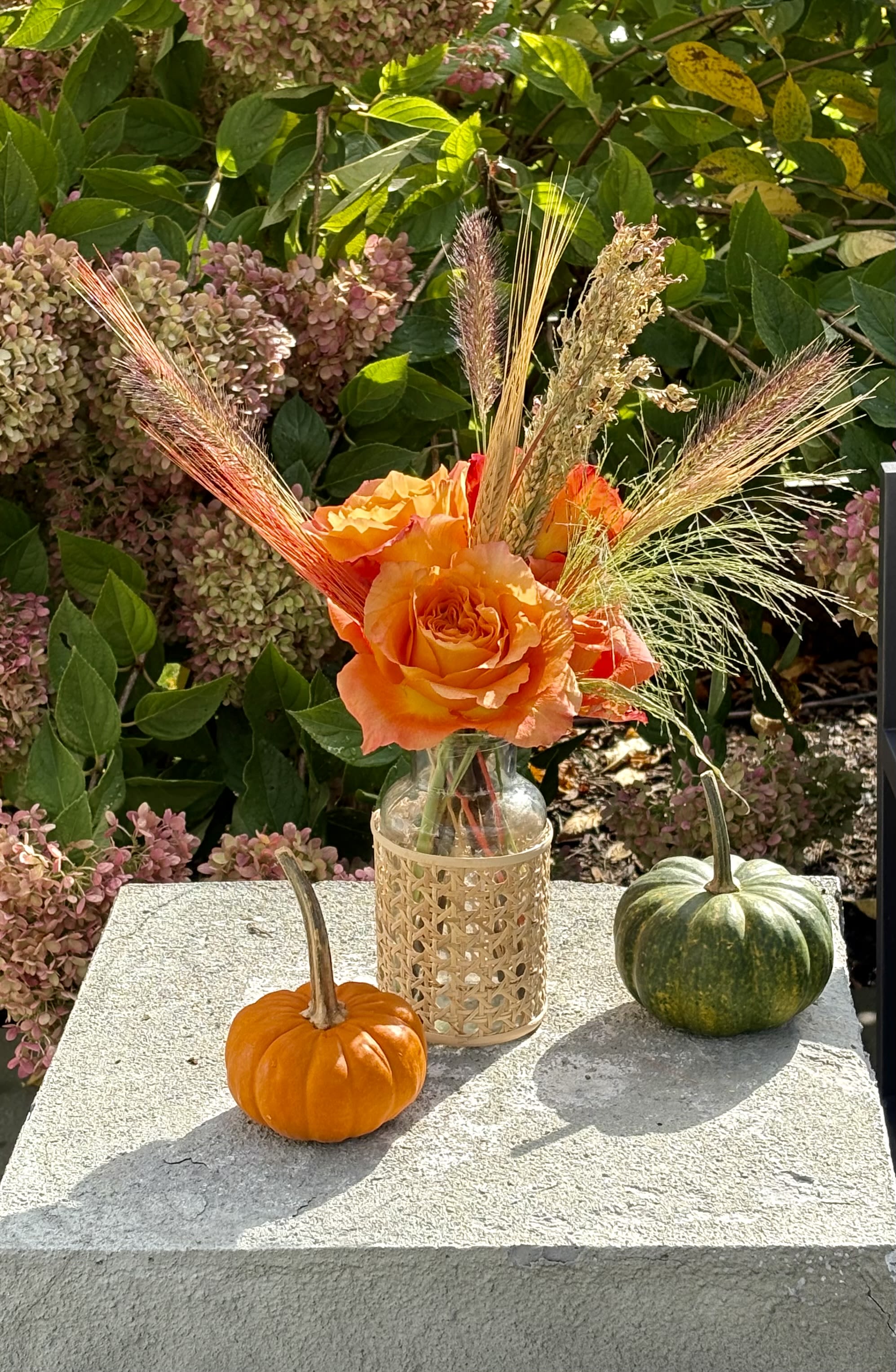 Orange rose arrangement in a glass bottle with pumpkins on a stone ledge