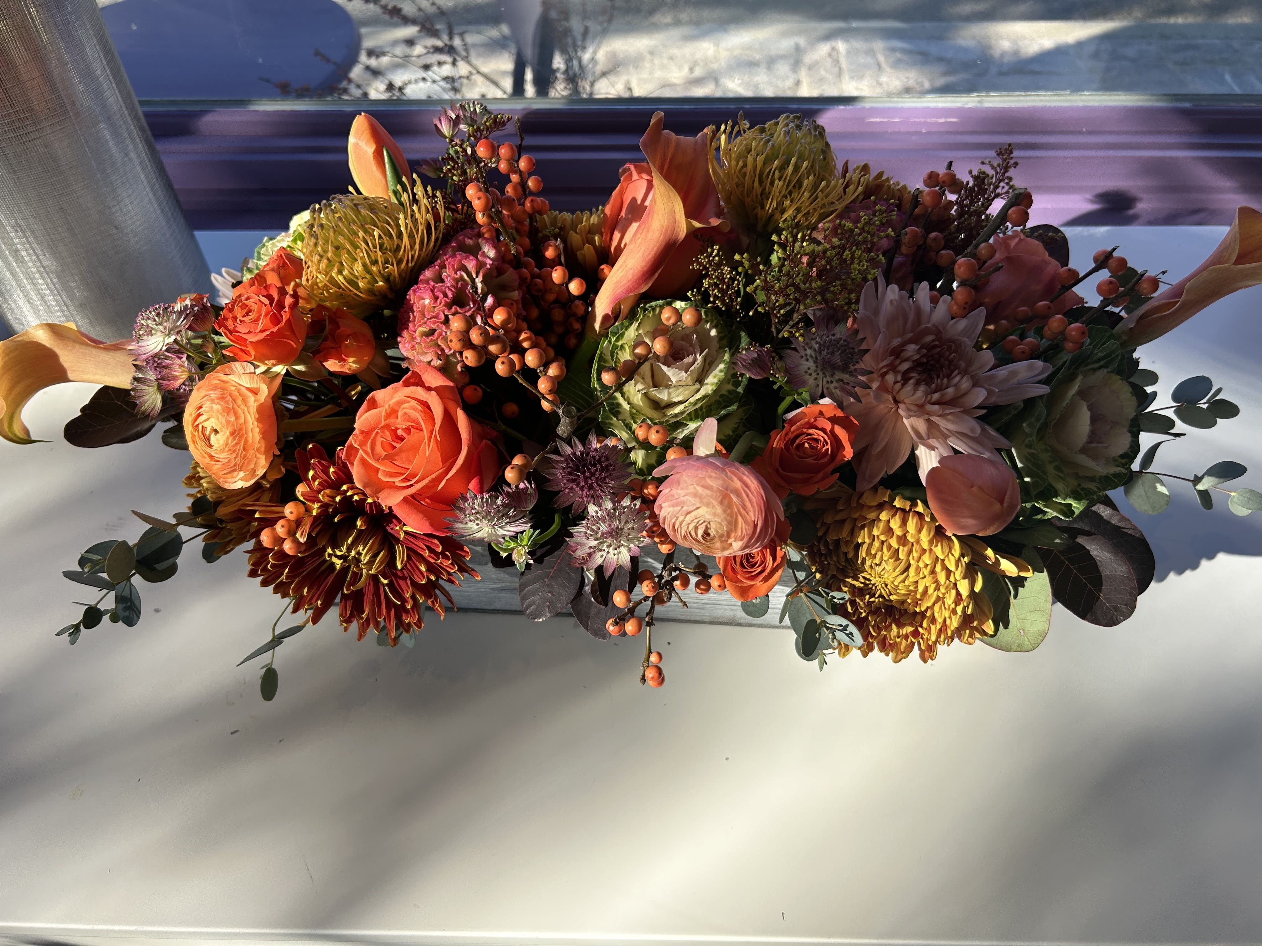 Low floral arrangement with orange and pink blooms in a rectangular container
