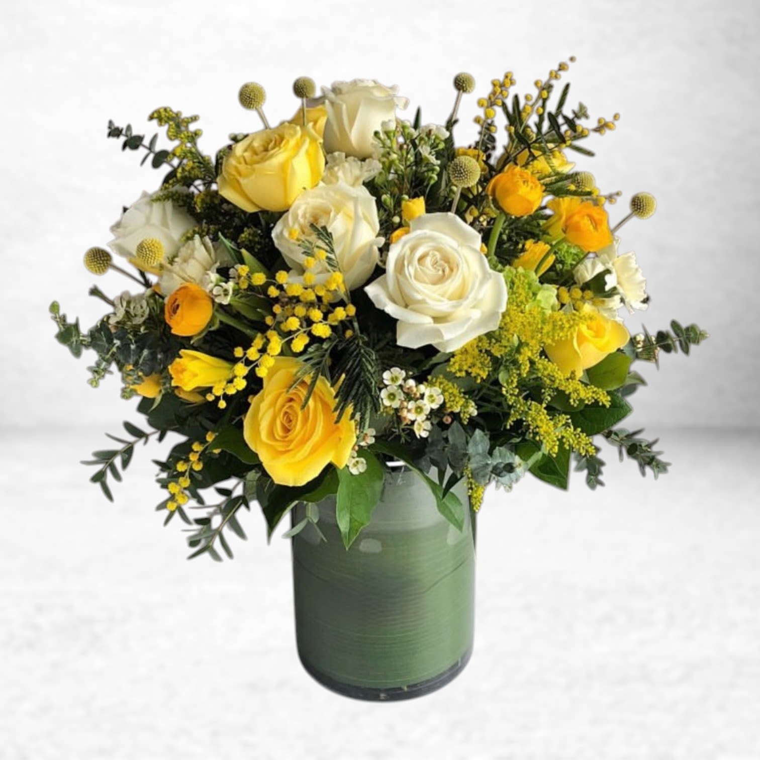 Sunny Shoreline Bouquet - Radiating warmth and joy, the Sunny Shoreline Bouquet combines buttery yellow roses, creamy white roses, golden ranunculus, mimosa, craspedia, and wild foliage in a sleek green vase. This sunny floral arrangement brings light and energy to birthdays, thank-you notes, and get well wishes across Galveston, Alvin, and Texas City.  We take pride in sourcing the freshest, highest-quality blooms. In the event that specific flowers are unavailable due to seasonal shifts or local supply, we will substitute with blooms of equal or greater value—always preserving the color palette, overall aesthetic, and integrity of the original design.