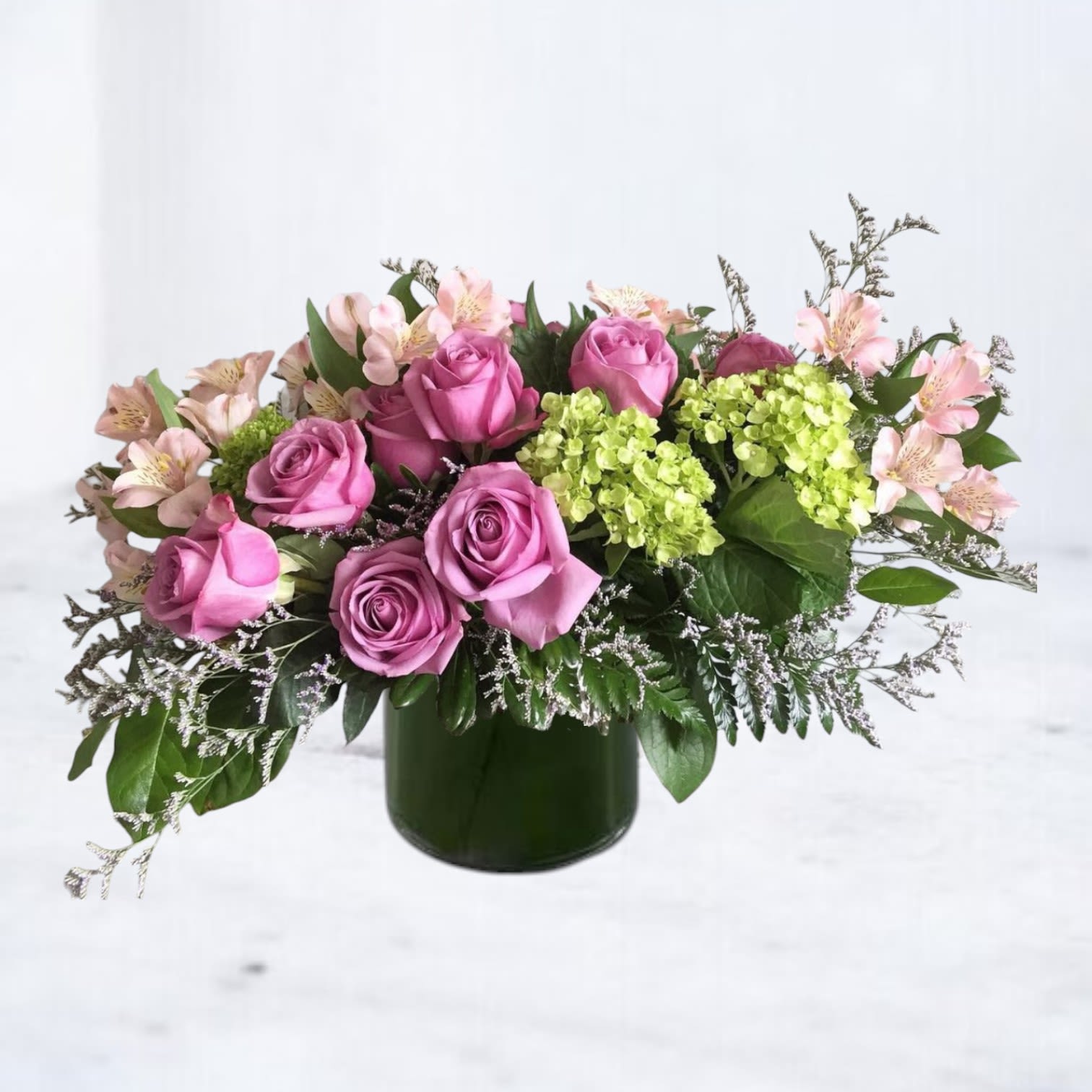 Lavender Meadow Bliss - Lavender Meadow Bliss features lush lavender roses paired with soft pink alstroemeria, delicate green hydrangea, and airy filler blooms. Designed in a modern leaf lined cylinder vase, this elegant arrangement offers a serene and uplifting touch, ideal for sympathy, thinking of you, get well soon, or just because. Hand-arranged by Twigs and Blooms and available for same-day delivery in Friendswood, League City, Dickinson, Galveston, Alvin, and nearby communities.  Substitution Policy: Twigs and Blooms is committed to using only the freshest flowers available. In rare cases, substitutions may be made to ensure timely delivery. Any substitutions will reflect the same overall design, color palette, and value.