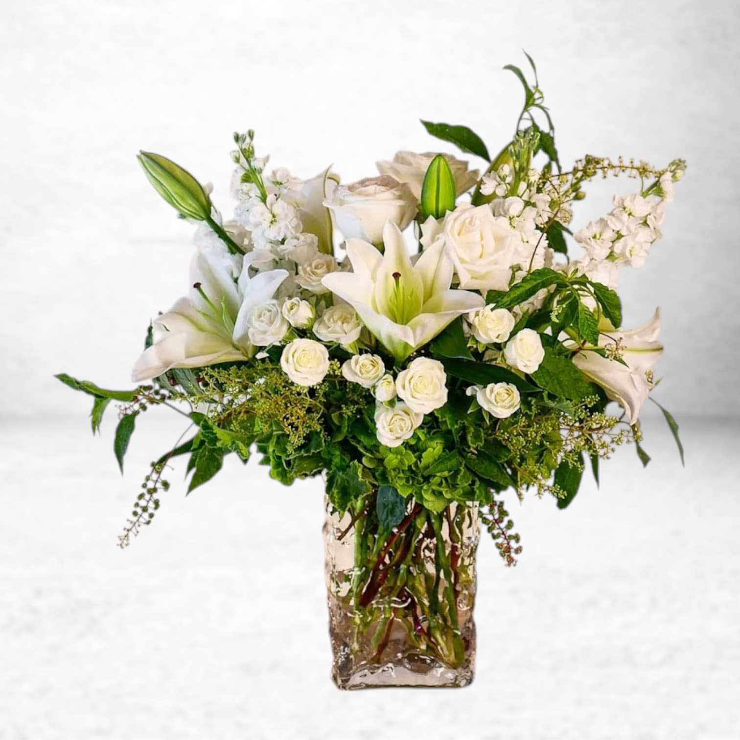 Ivory Cascade - The Ivory Cascade arrangement radiates timeless grace with its elegant display of pristine white lilies, roses, spray roses, hydrangeas, and lush greenery. Designed in a tall textured glass vase, this sophisticated bouquet is perfect for sympathy tributes, weddings, anniversaries, or any occasion that calls for pure, refined beauty. Handcrafted by Twigs and Blooms in Friendswood, Texas, this luxurious design is available for same-day flower delivery in Friendswood, League City, Dickinson, Alvin, Galveston, and surrounding areas. Trust our expert florists to deliver a serene and stunning floral statement with every order.  Substitution Policy: At Twigs and Blooms, each arrangement is custom-designed with the freshest available blooms. On rare occasions when certain flowers are unavailable, we will substitute with equally beautiful blooms of comparable color, value, and style to maintain the integrity of the design.