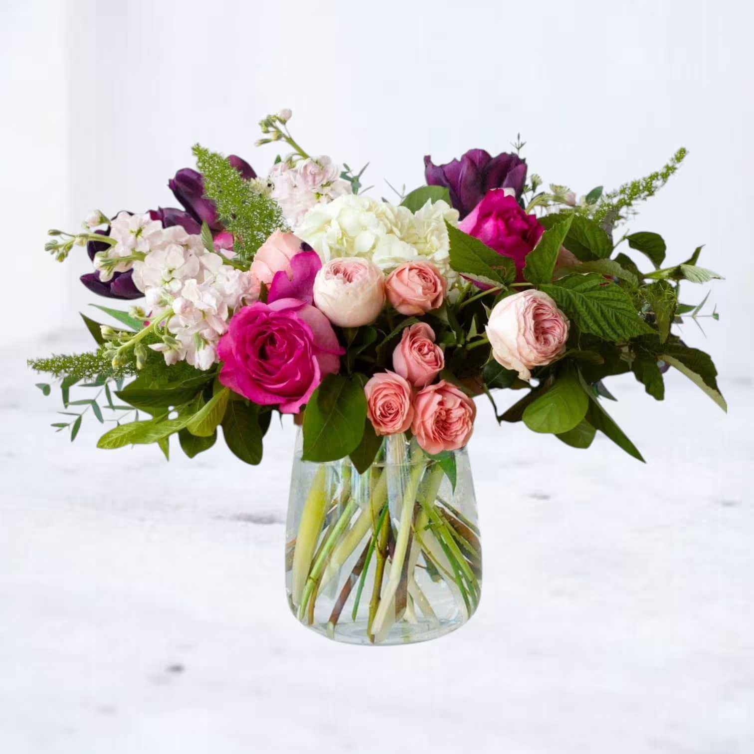 Mixed pink, white, and purple flowers arranged in a clear glass vase