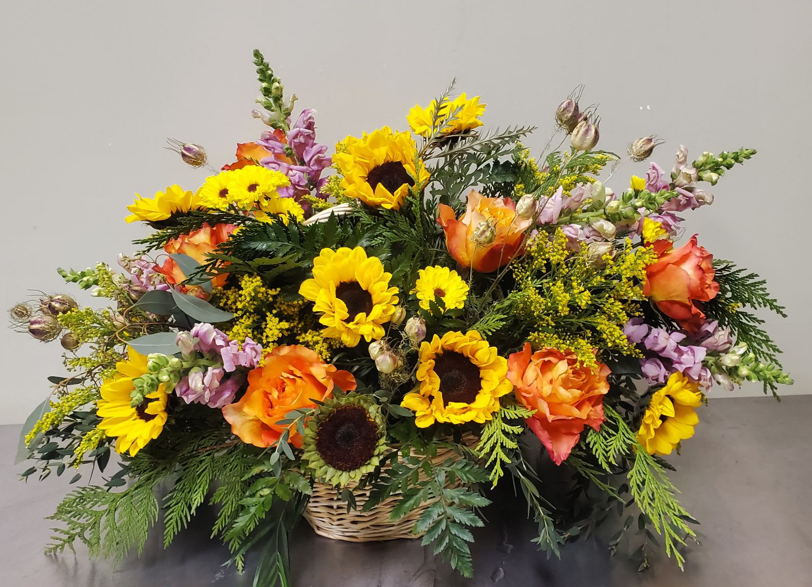 Basket arrangement of sunflowers, orange roses, and purple snapdragons
