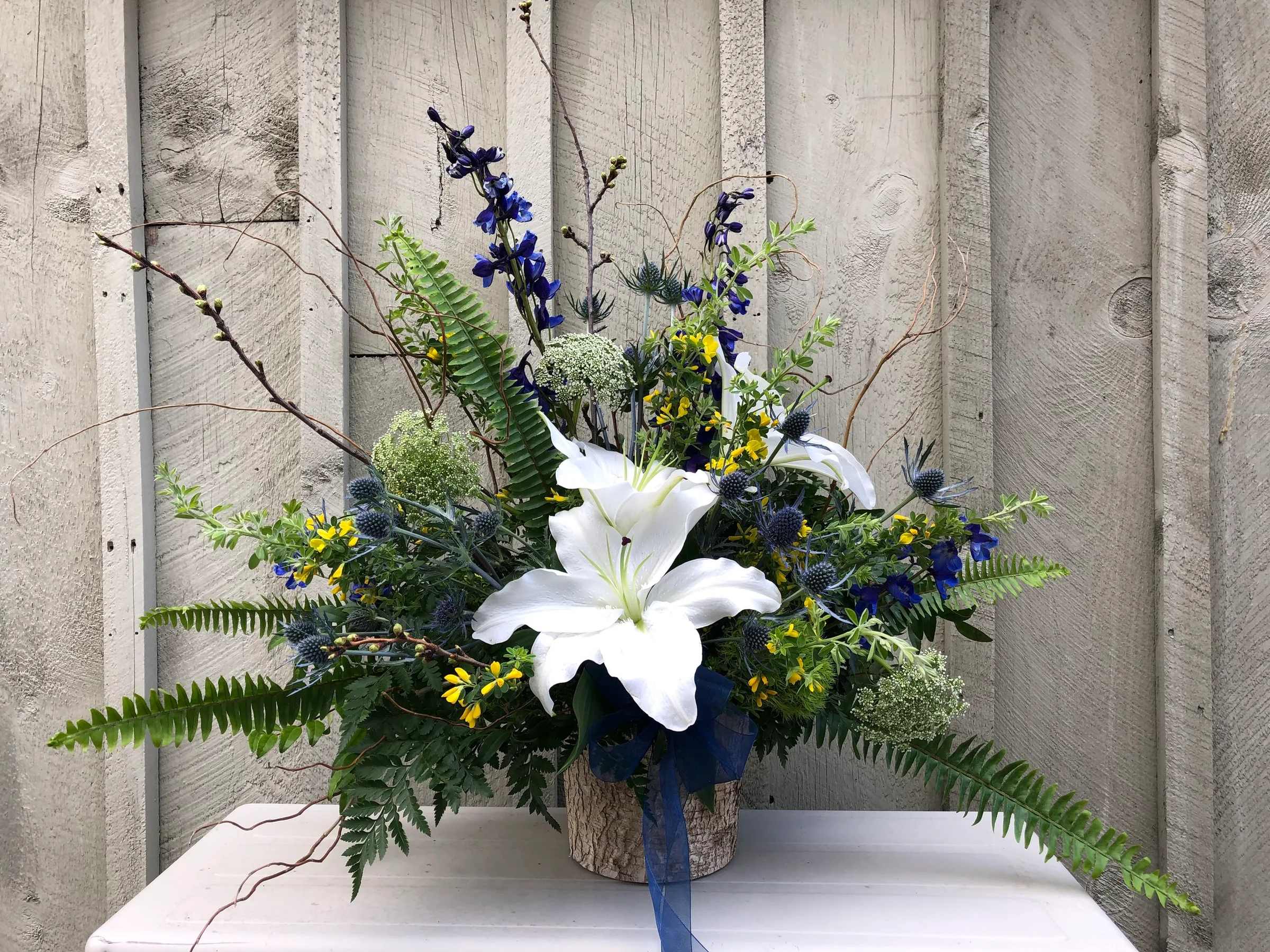White lilies in a rustic container with blue and yellow flowers