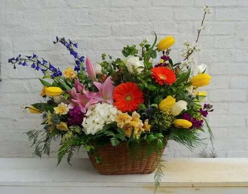Mixed flower arrangement in a wicker basket with pink, yellow, white, and orange blooms