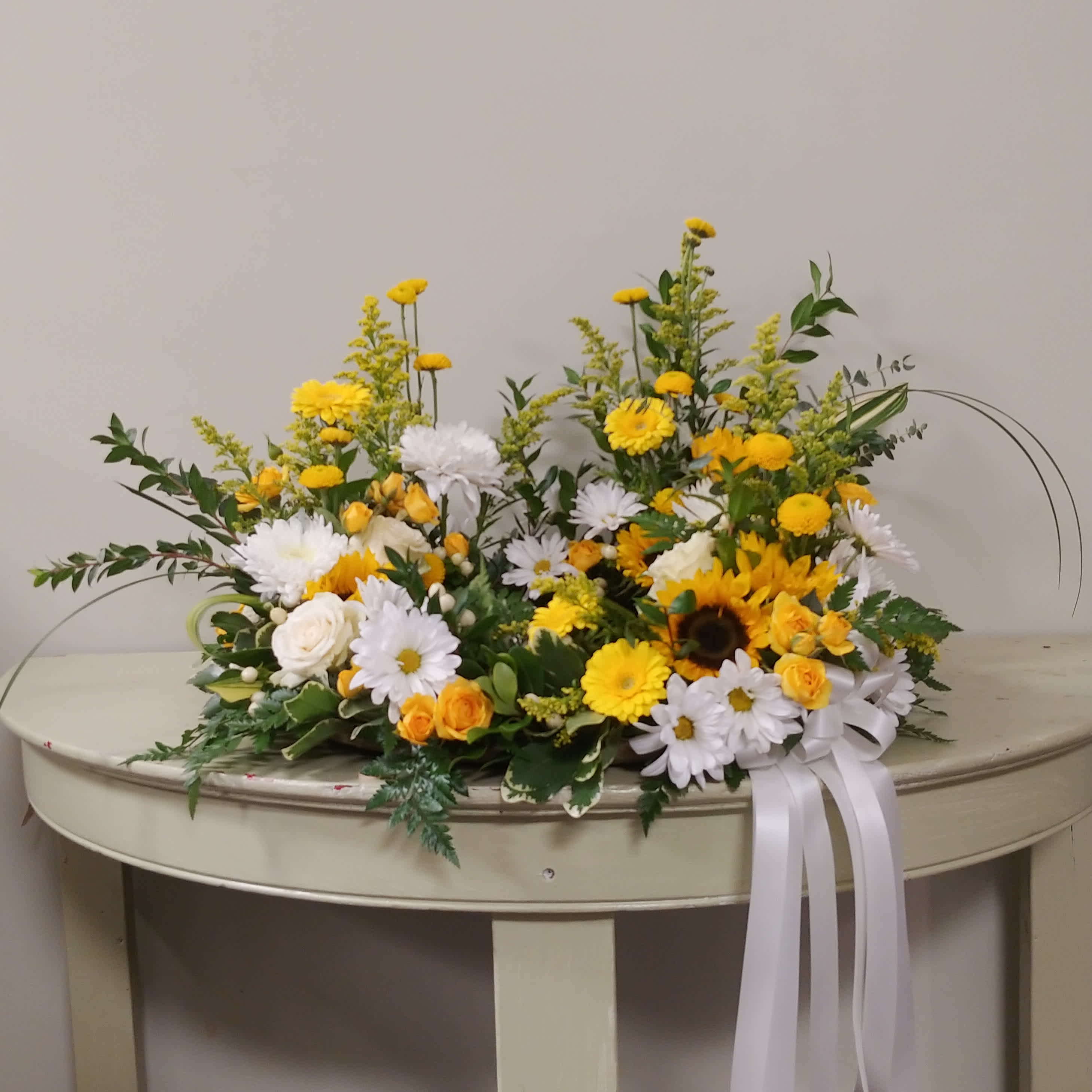 Yellow and white floral arrangement on a table with a white ribbon