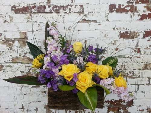 Yellow and purple roses arranged in a rustic basket