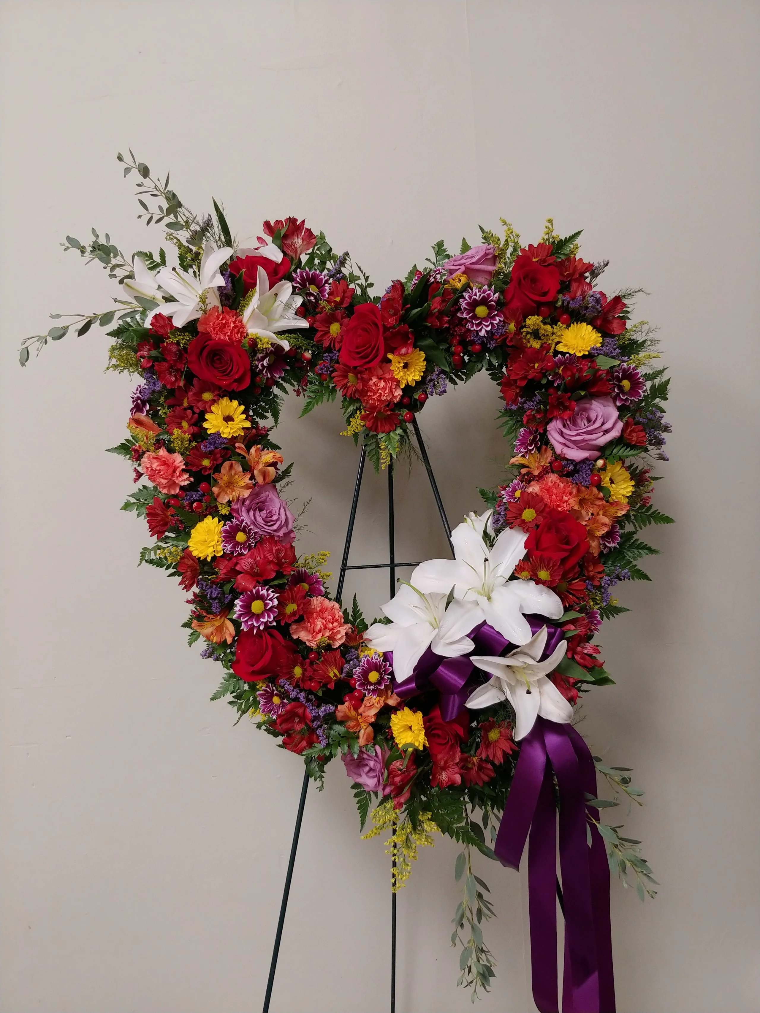 Heart-shaped floral wreath with red, white, and purple flowers on a stand