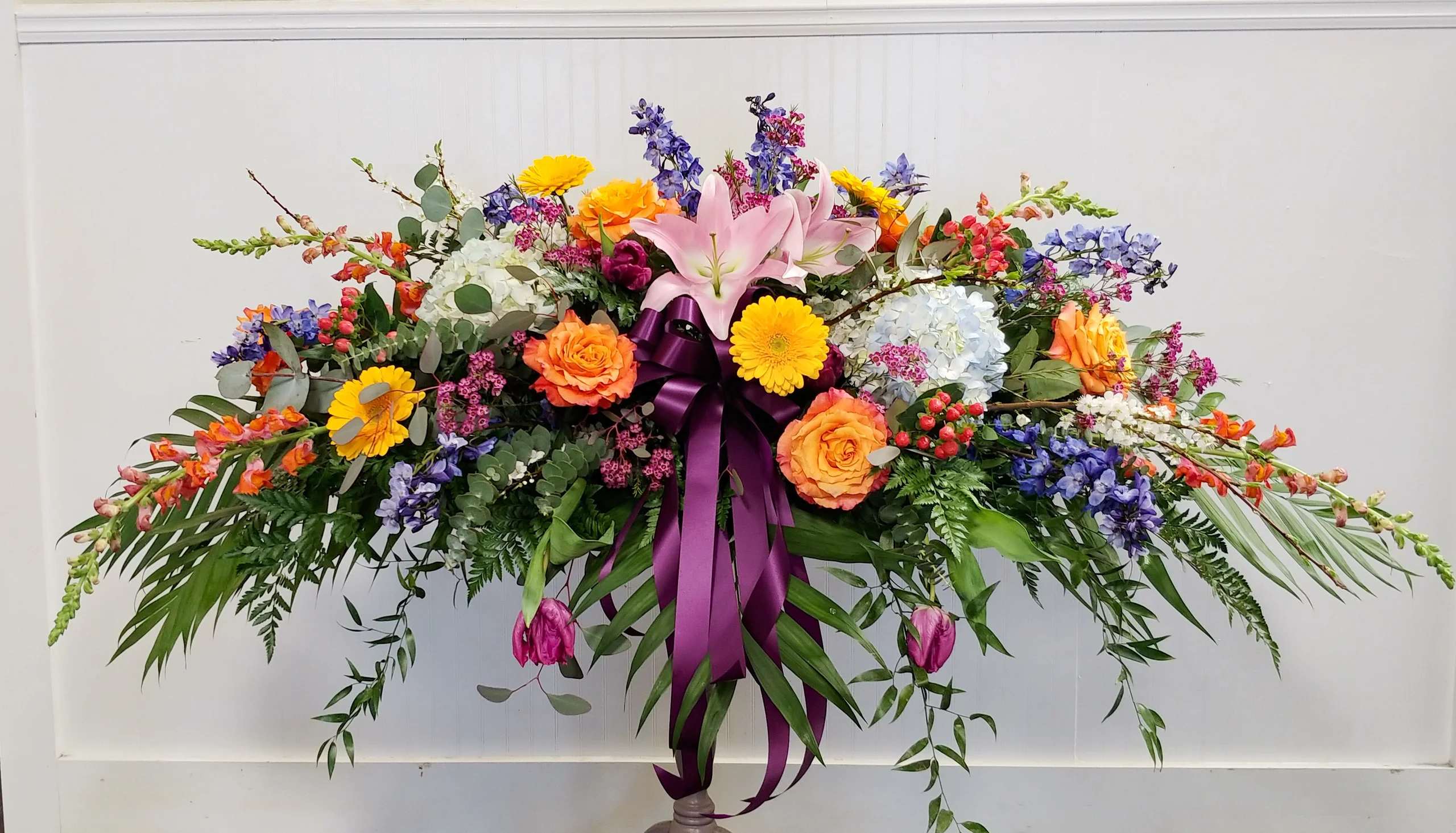 Large colorful floral spray with lilies, roses, and a purple ribbon