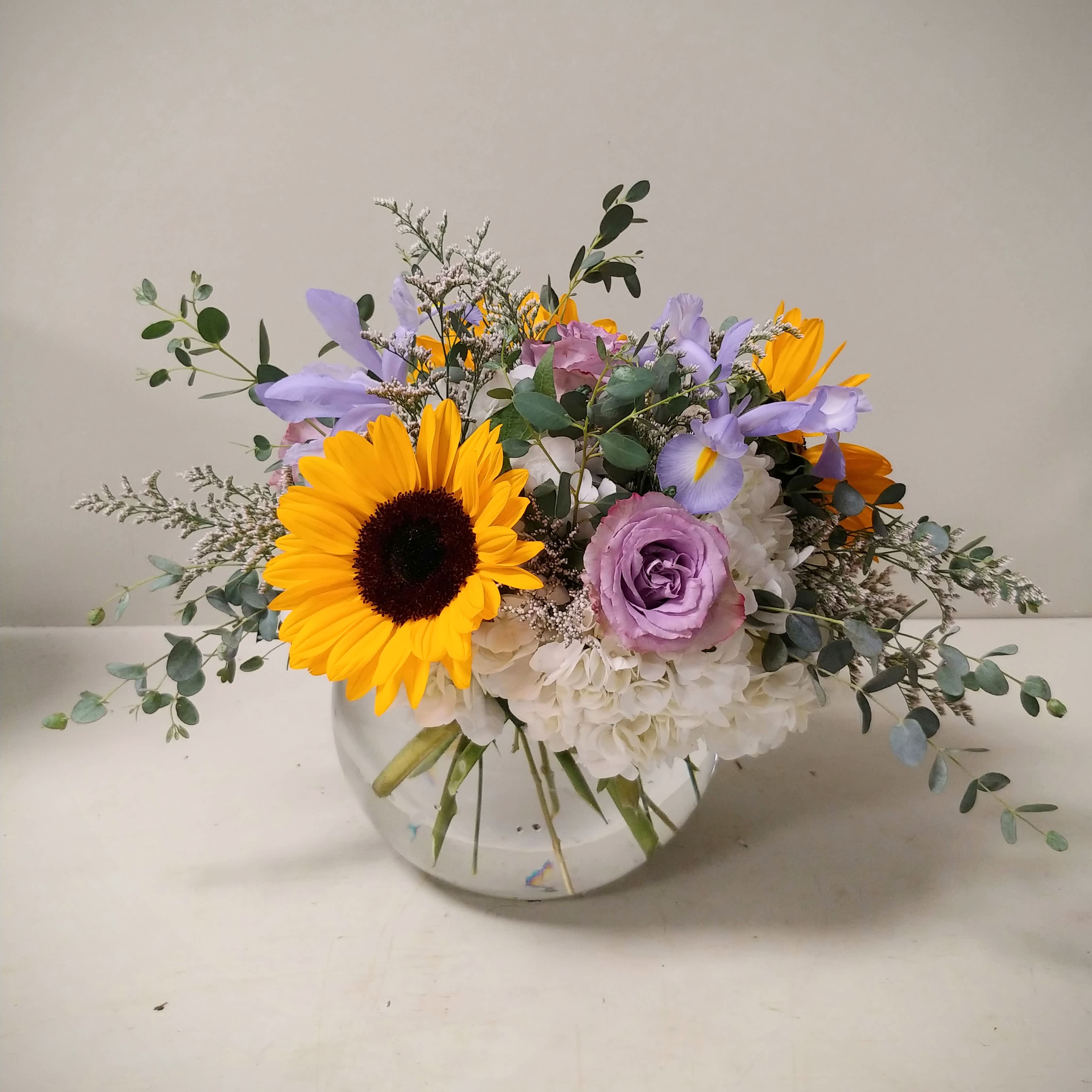 Sunflower and Lavender Bubble Bowl - A low and lush bubble bowl filled with Sunflowers, Roses, Hydrangea and seasonal florals like Iris and Eucalyptus.  Please Note: Each design is custom made and filled to value. We only use fresh product to ensure top quality so new orders are subject to substitutions. Call the shop at 845-247-3164 and one of our Floristas will happily let you know what is currently available.