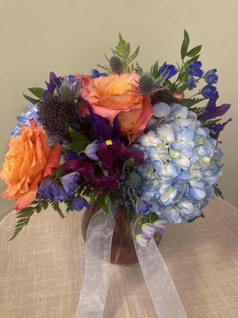 Bouquet of orange, blue, and purple flowers in a vase with ribbon