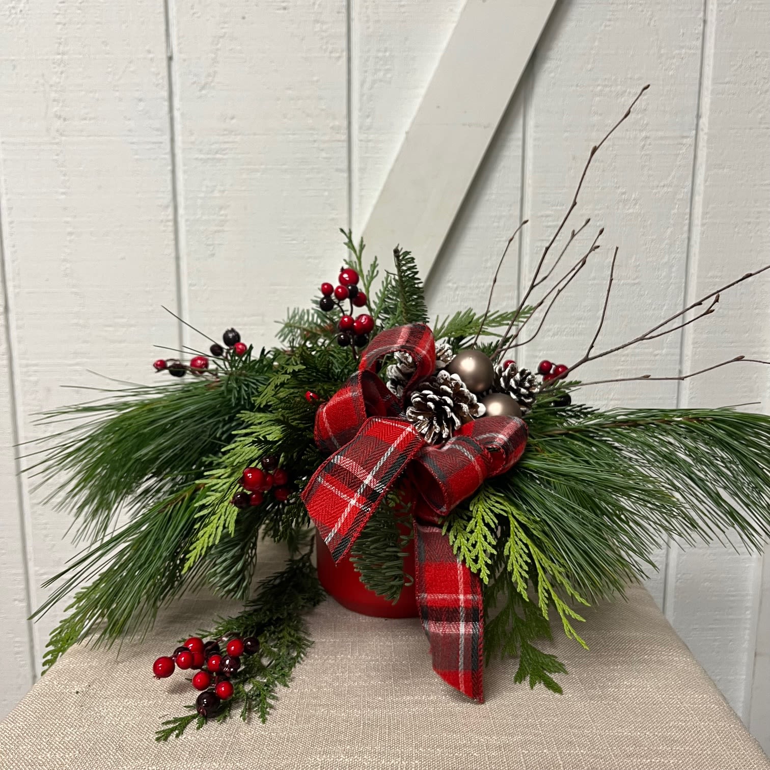 Holiday arrangement with pine, berries, pinecones, and a red plaid ribbon in a red container