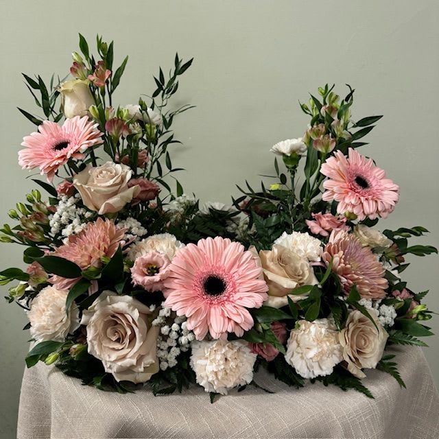 Pink gerbera daisies and cream roses arranged in a low floral display