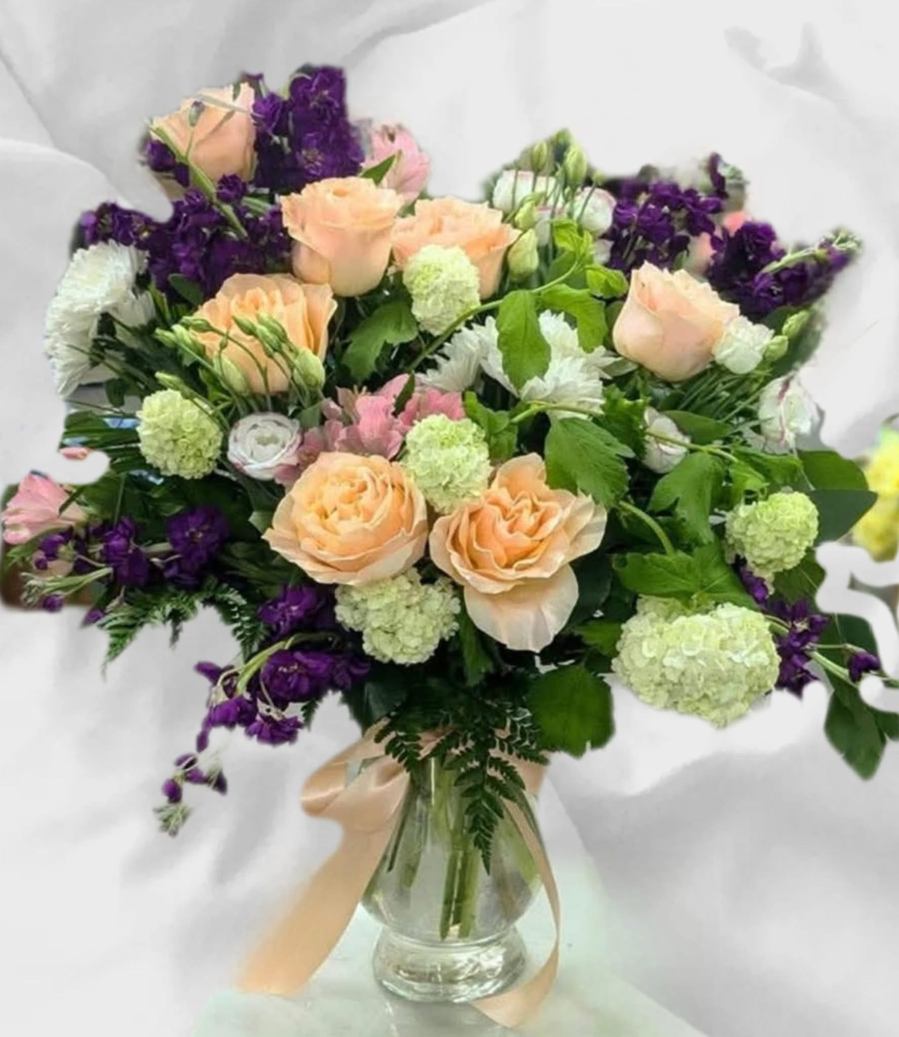 Peach roses and purple flowers in a glass vase with a ribbon