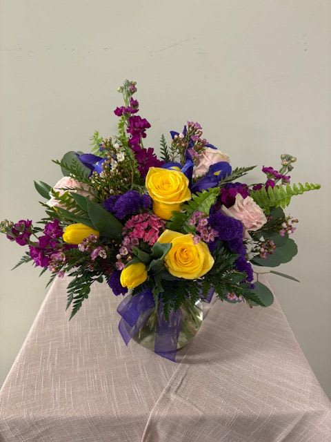 Bouquet of yellow and purple flowers in a glass vase with a ribbon