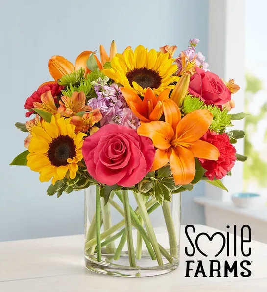 Bright mixed bouquet with sunflowers, orange lilies, and pink roses in a clear glass vase