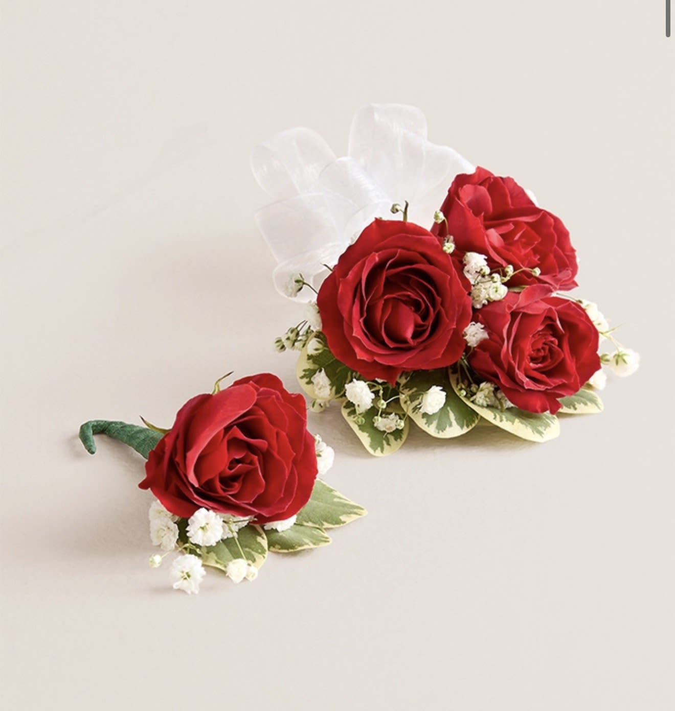 Red Corsage &amp; Boutonniere (White Bow) - This elegant corsage and boutonniere set, featuring vibrant red blooms, is thoughtfully designed to pair perfectly, creating a polished and harmonious look for any special occasion. Each piece showcases carefully selected red flowers and accents, offering a timeless and refined touch that complements your ensemble beautifully.