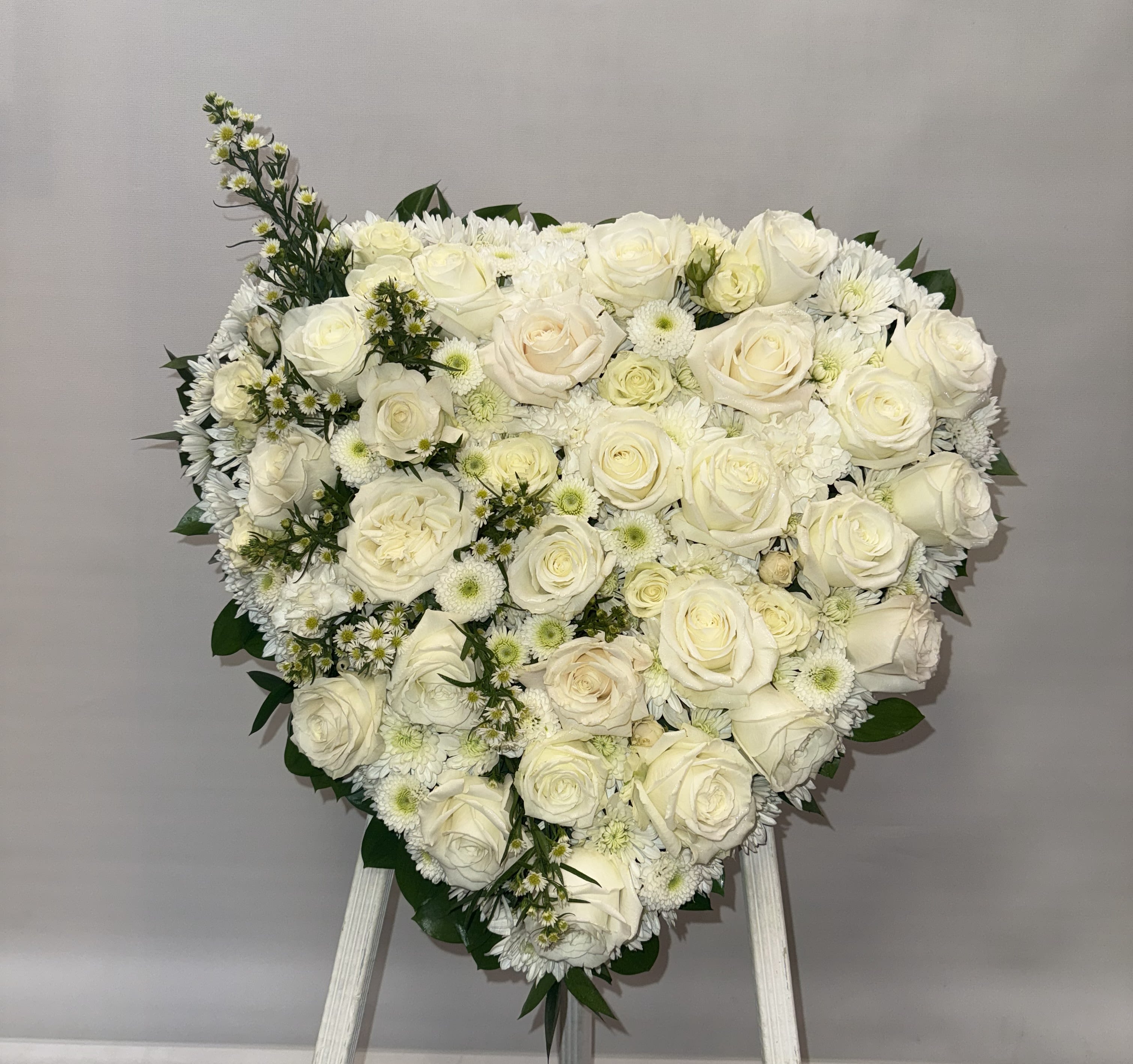 Heart-shaped arrangement of white roses and daisies on an easel