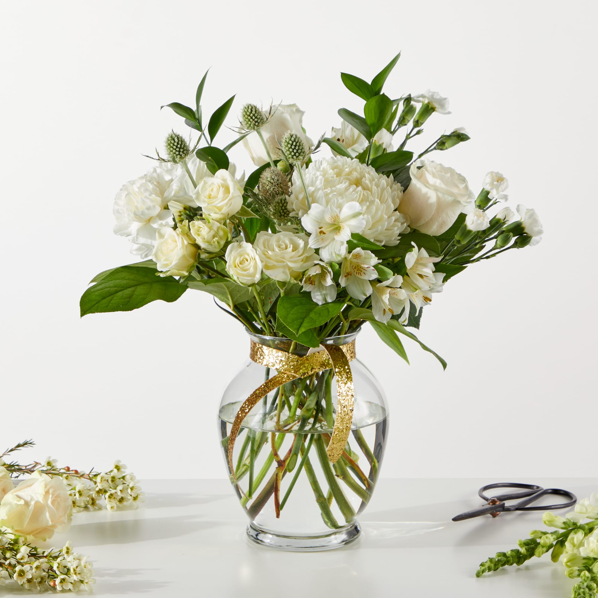 White floral bouquet in a clear glass vase with a gold ribbon