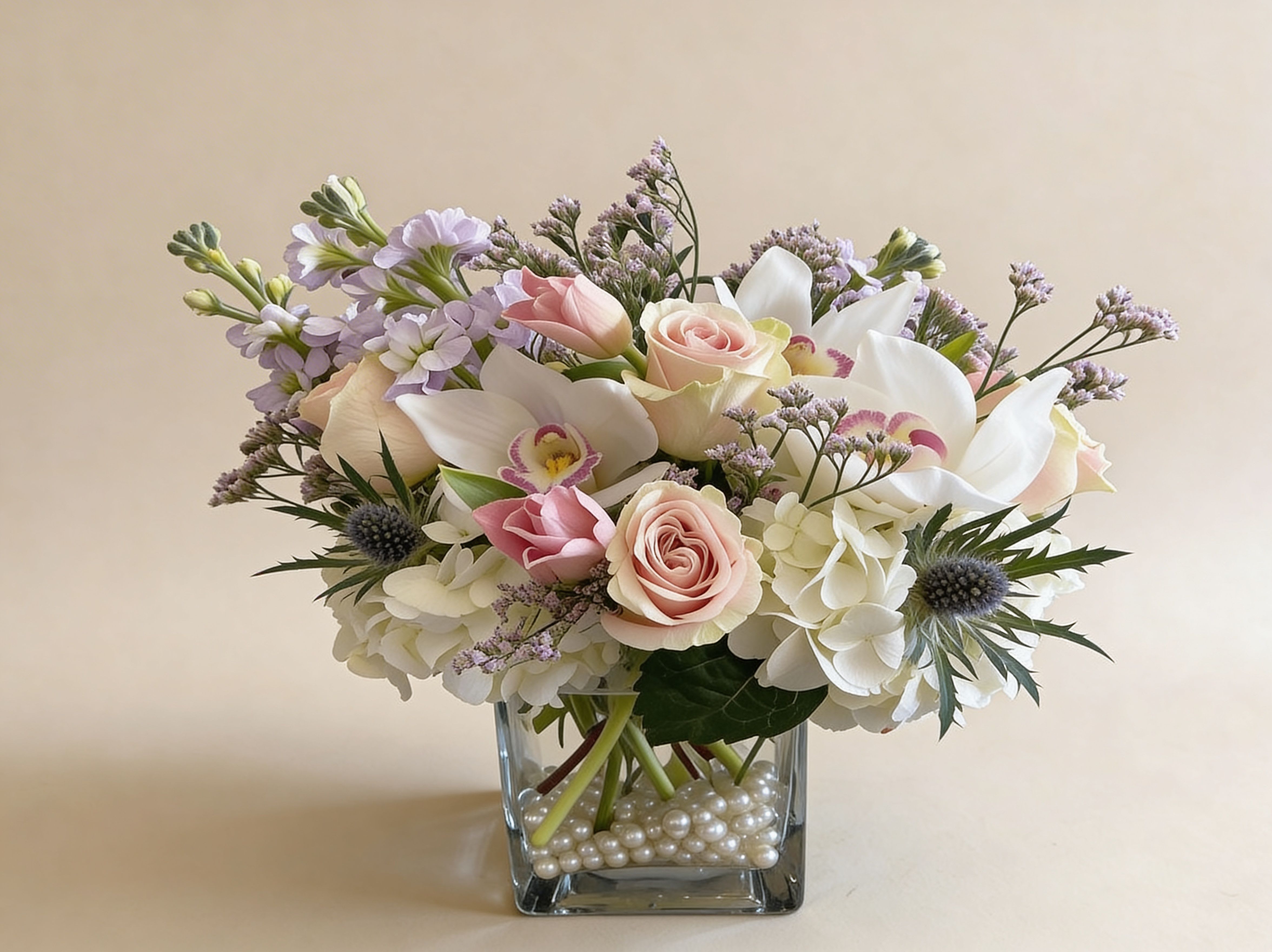 Pastel arrangement of roses, orchids, hydrangeas and stock in a square glass vase with pearl accents