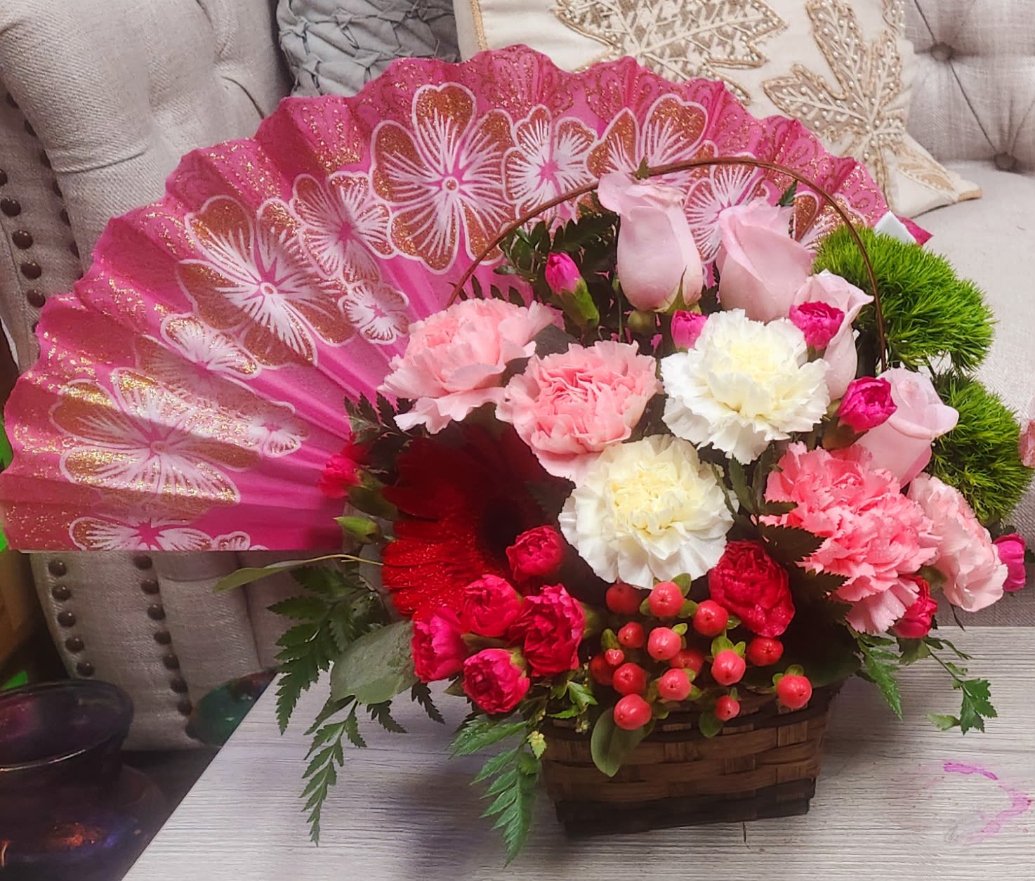 Pink floral arrangement in a basket with a decorative fan backdrop