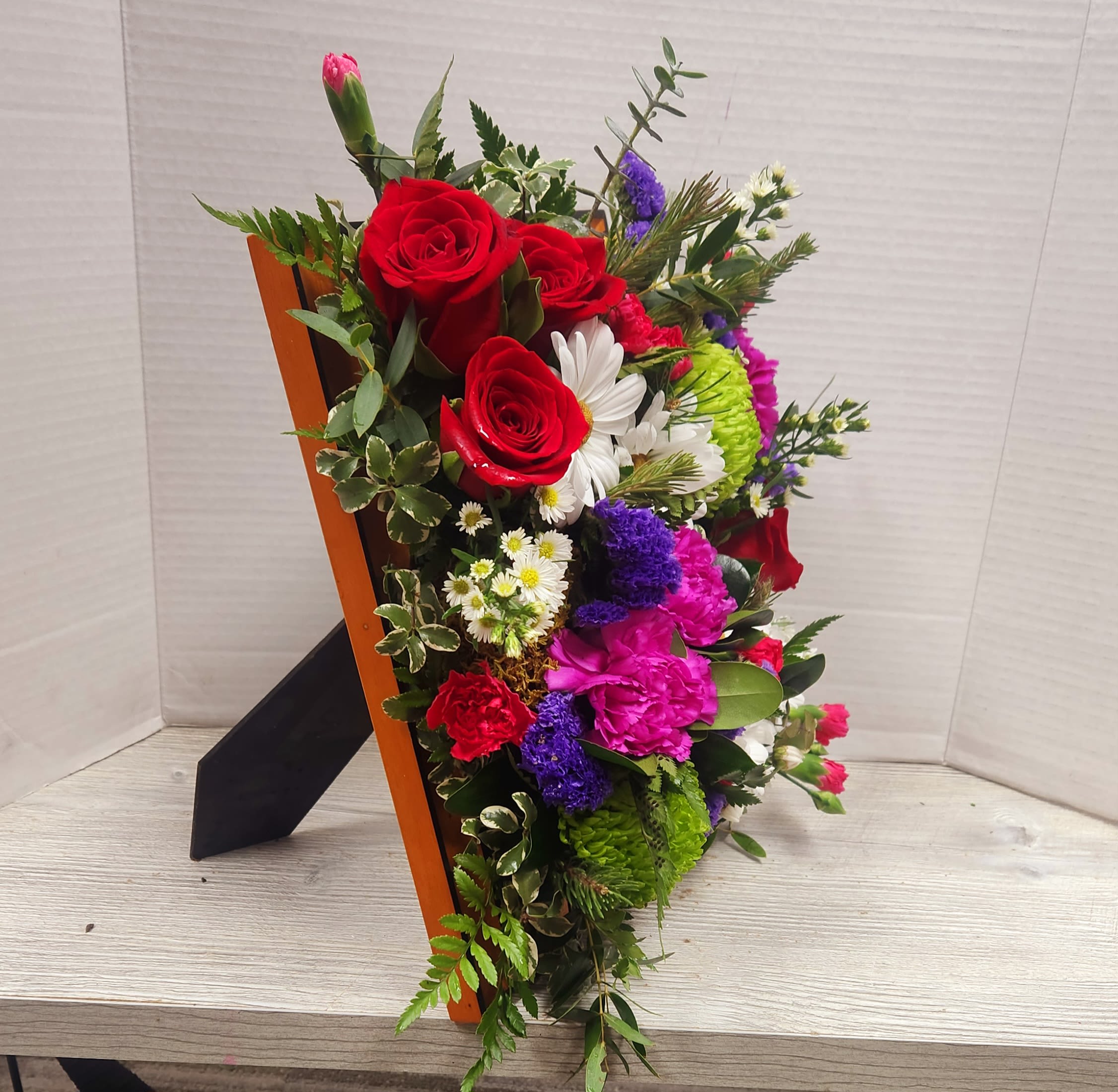 Mixed bouquet with red roses, pink carnations, and white daisies in a wooden holder
