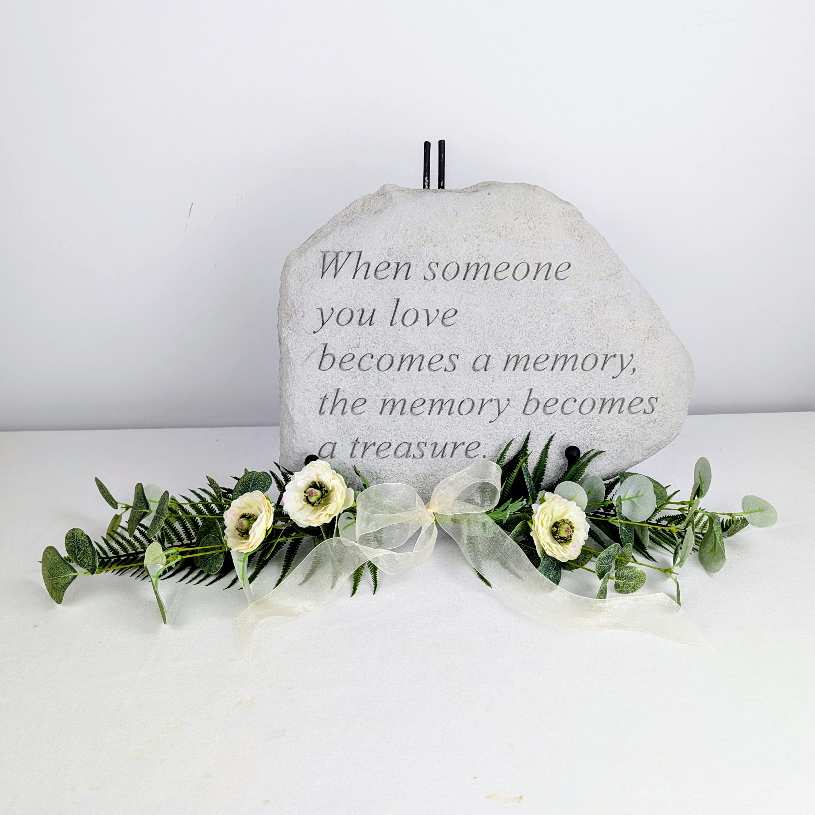 Memorial stone with white flowers and greenery arranged at the base