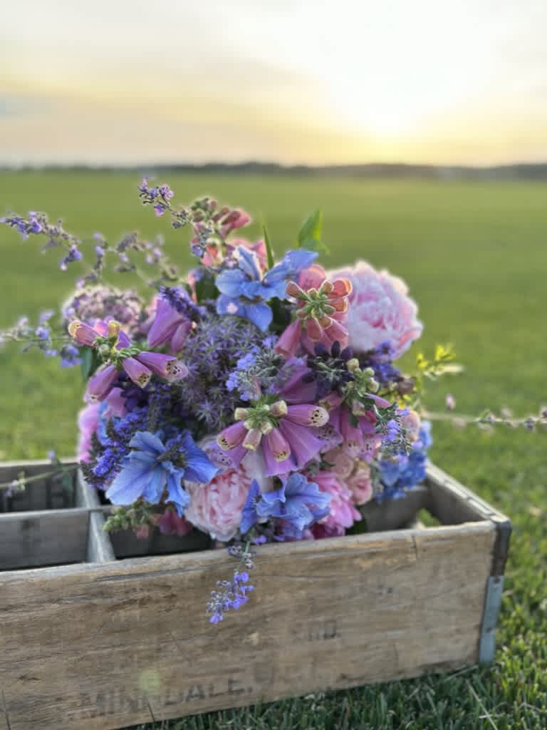 Mixed bouquet of blue, pink, and purple flowers in a wooden crate