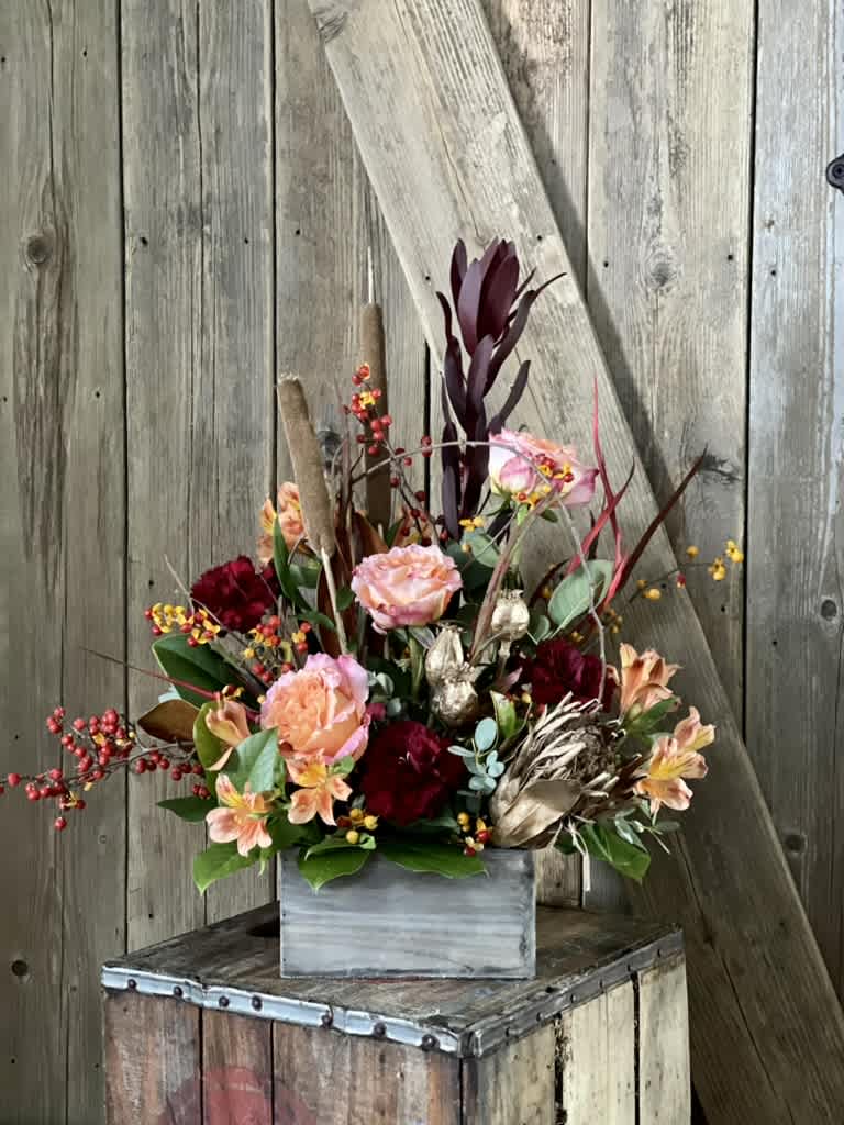 Mixed floral arrangement in a gray wooden box with burgundy and peach blooms